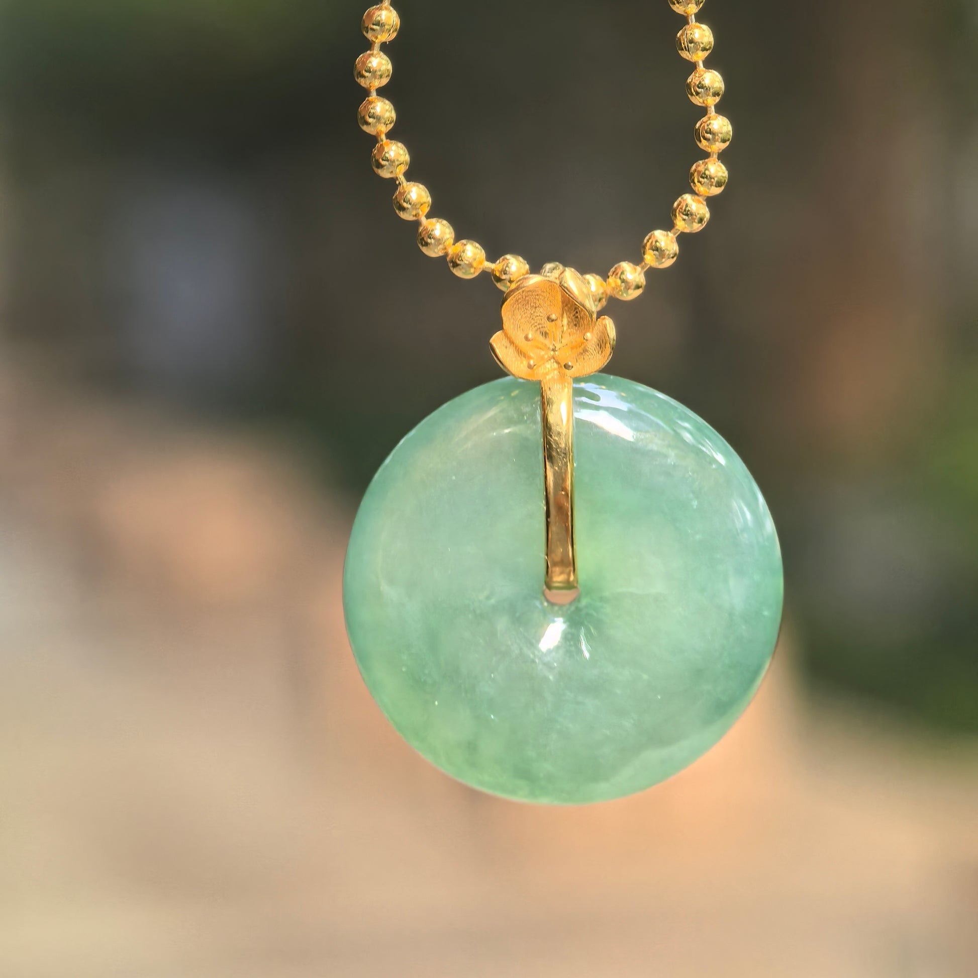 Natural Grade-A icy glutinous light green jadeite Peace Pendant hanging from a gold-tone beaded chain with an 18K gold flower bail.