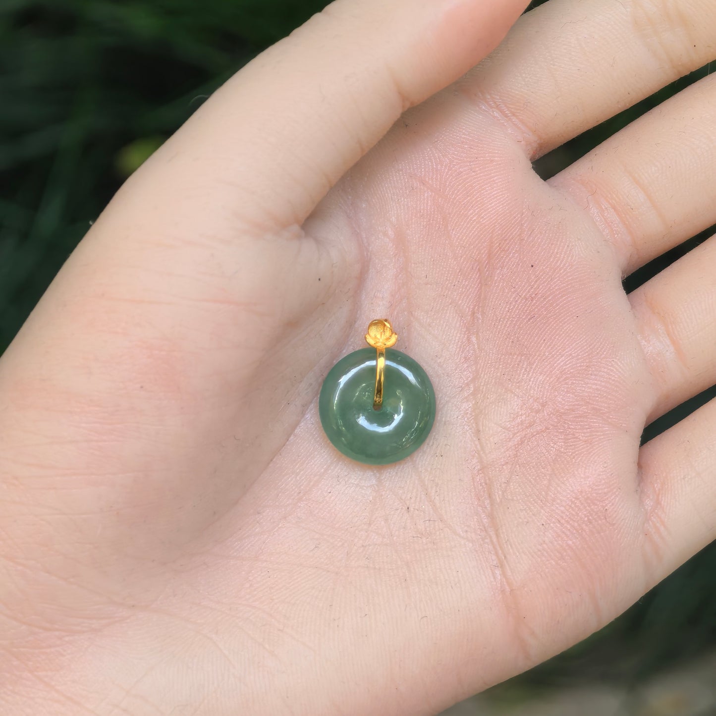 Hand-held view of the petite light green jadeite Peace Pendant showing its compact round proportions and gold fitting.