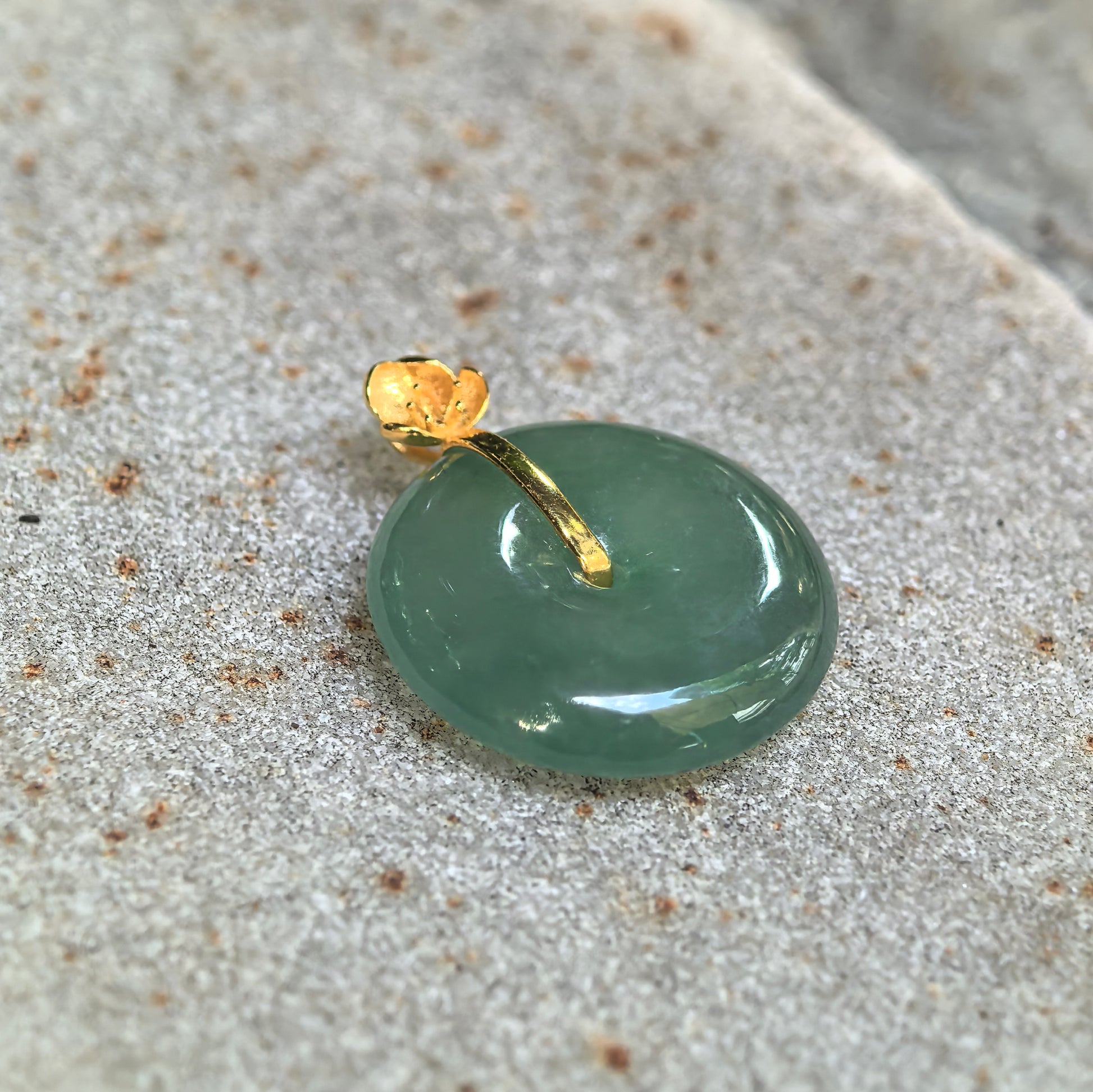 Close-up side view of the light green jadeite Peace Pendant showing its rounded profile, polished surface, and 18K gold connector.