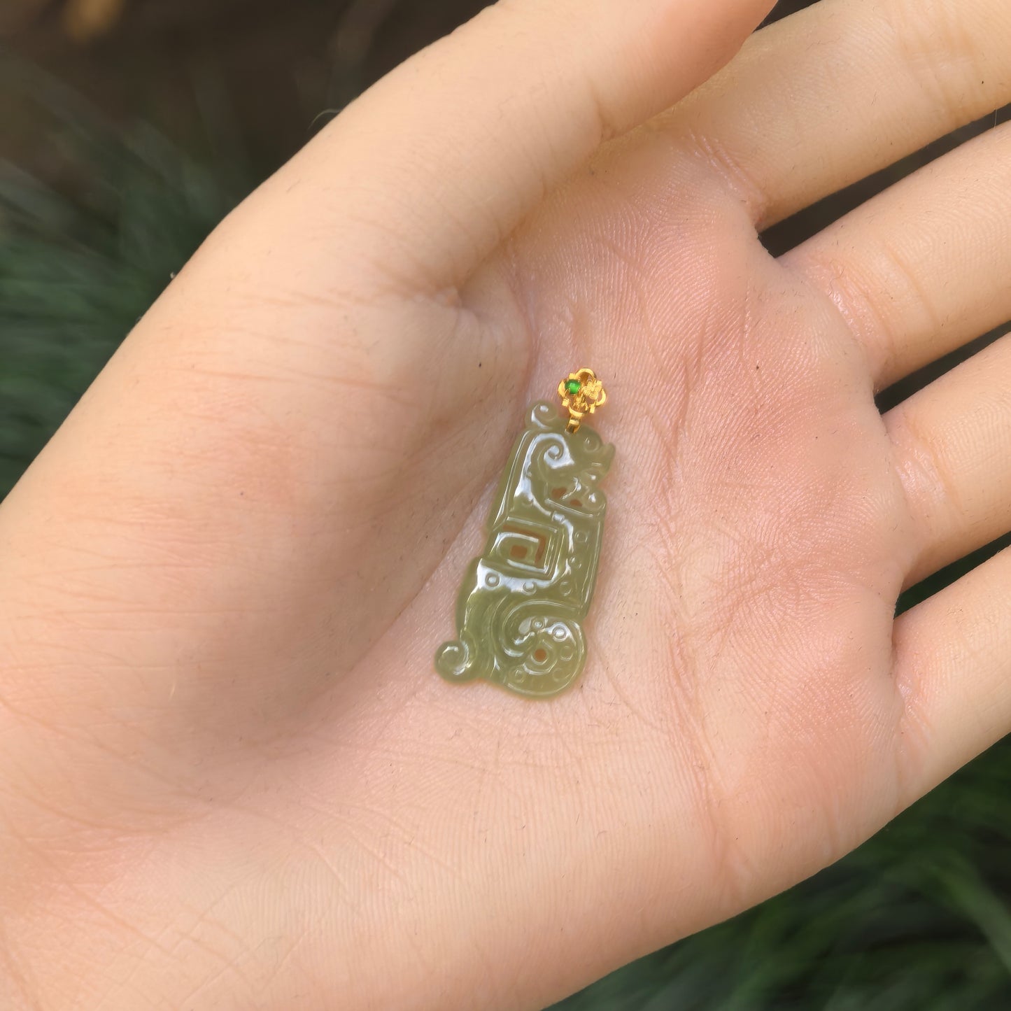 Hand-held view of the petite yellow-green jadeite pendant showing its elongated archaic Kui dragon carving.