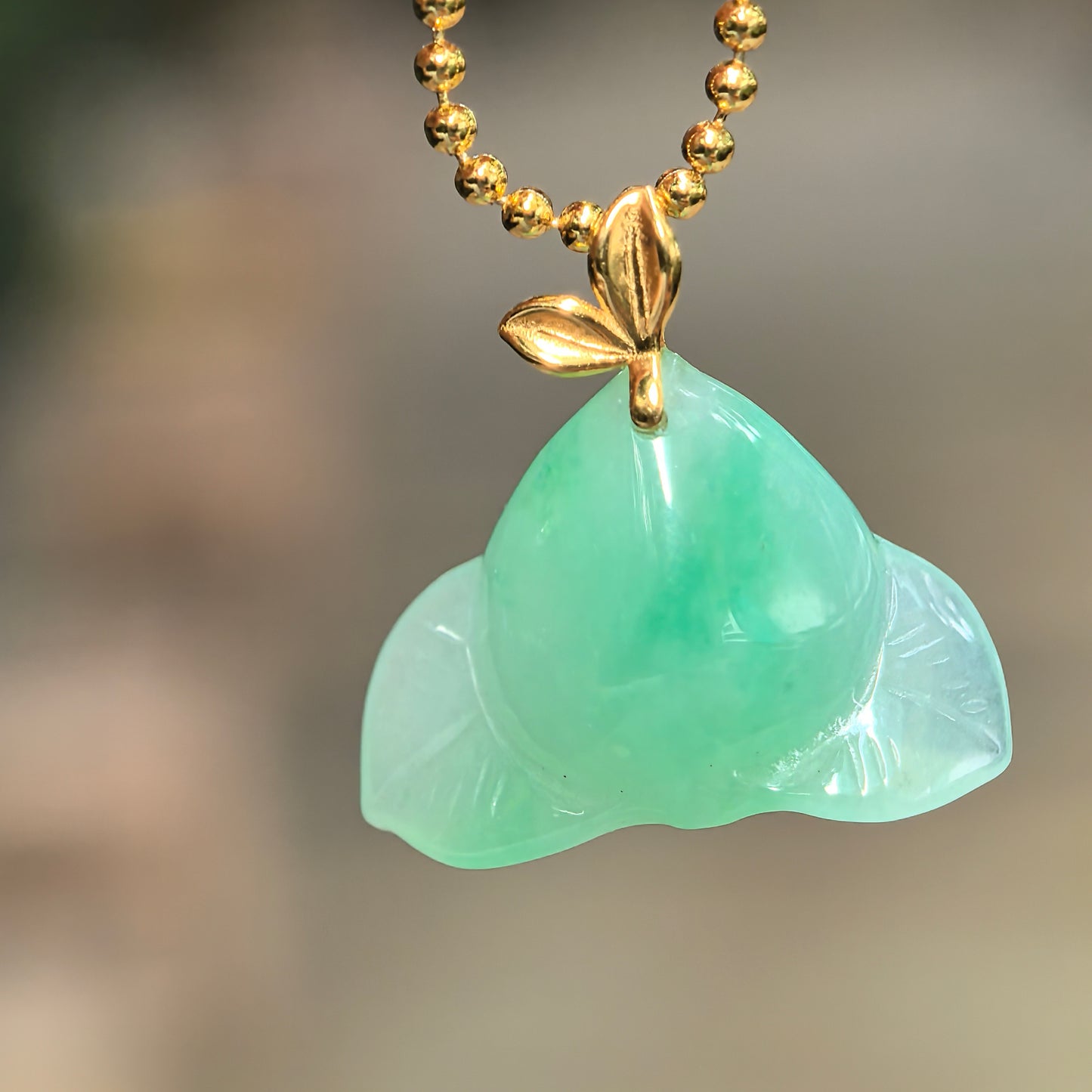 Natural Grade-A icy glutinous green peach jadeite pendant with an 18K gold leaf bail hanging from a gold-tone chain.