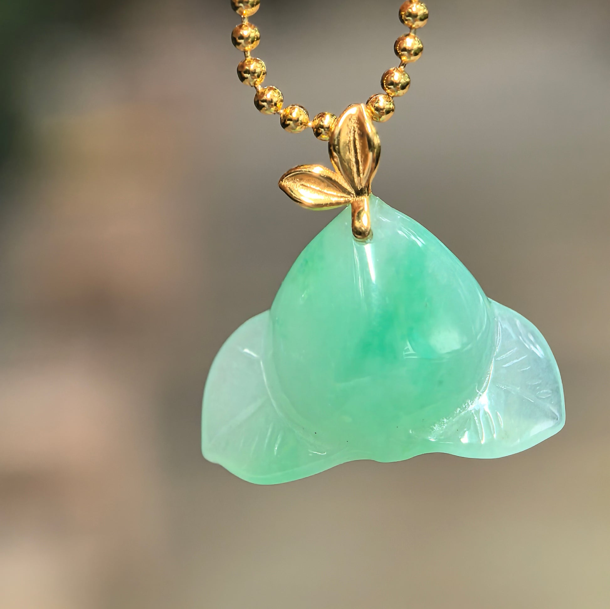 Natural Grade-A icy glutinous green peach jadeite pendant with an 18K gold leaf bail hanging from a gold-tone chain.