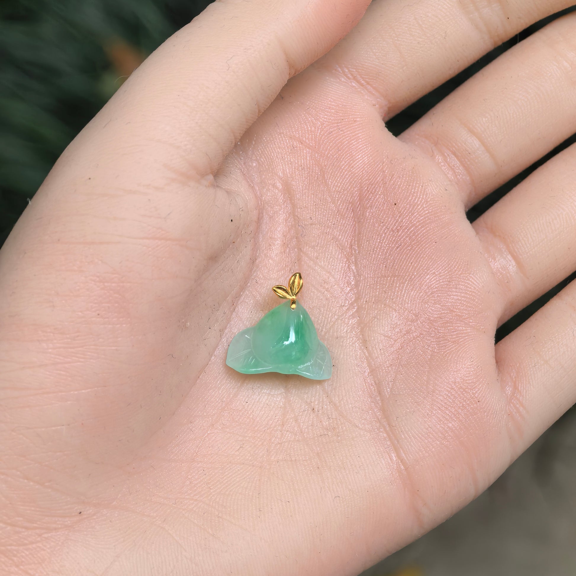 Hand-held view of the petite green peach jadeite pendant showing its compact three-dimensional proportions.
