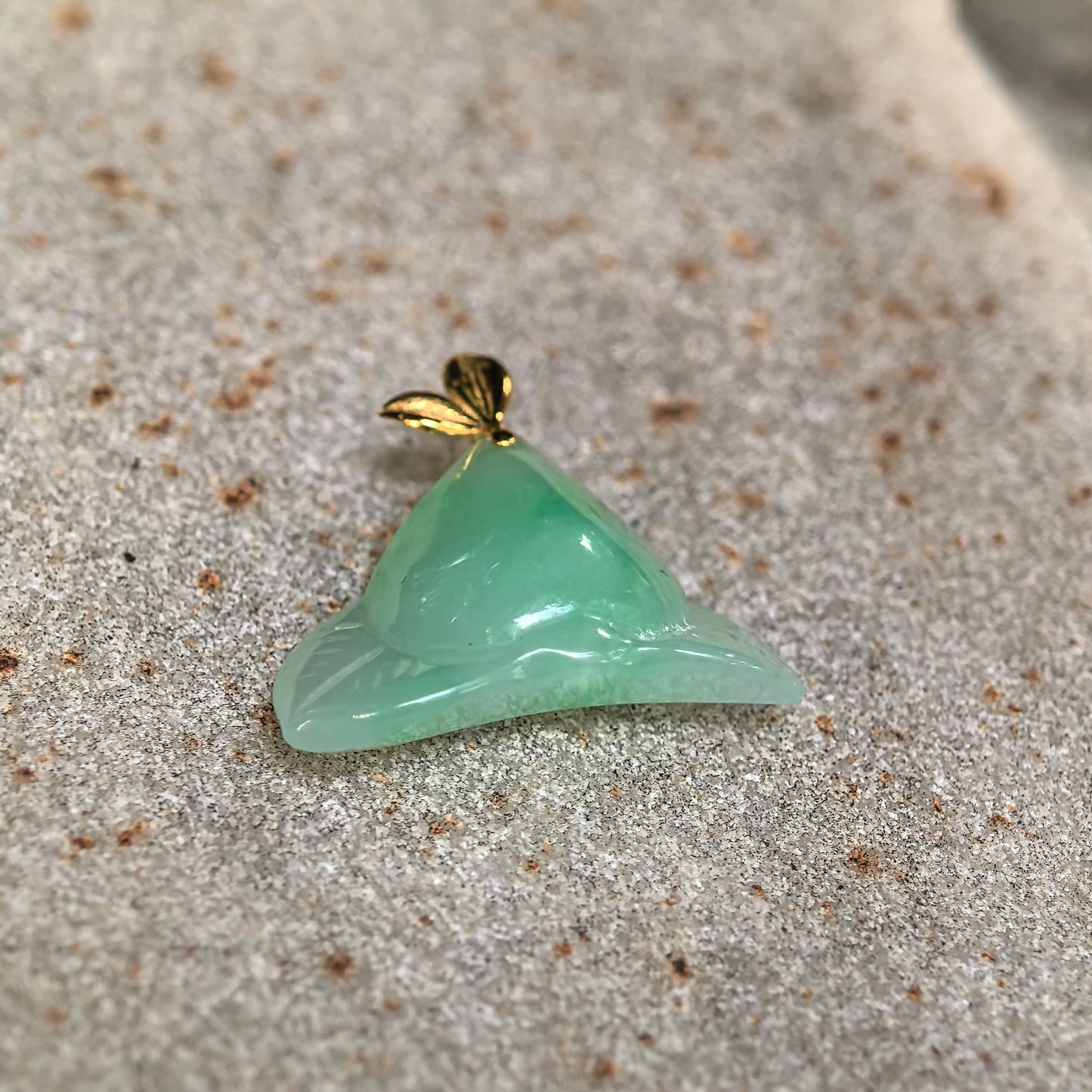 Close-up of the green jadeite peach pendant showing its rounded carving, leaf details, and smooth translucent texture.