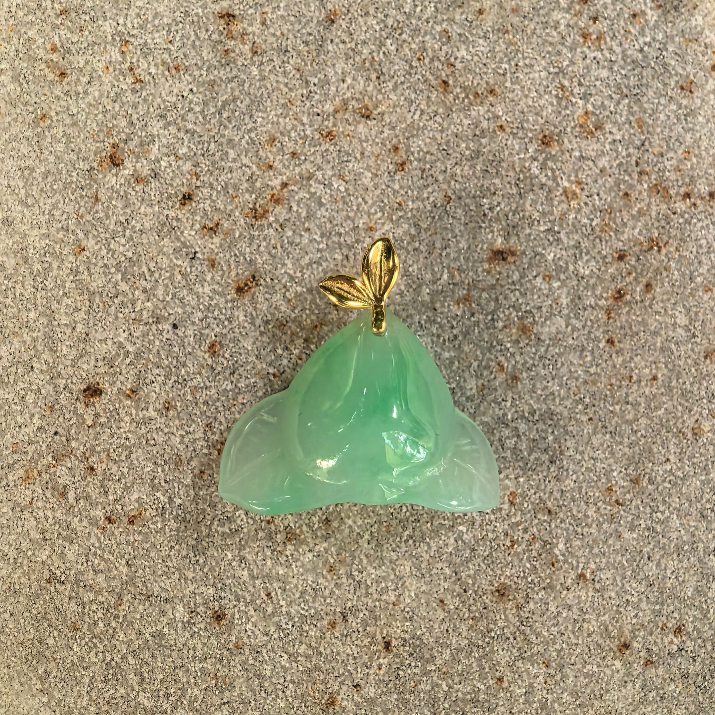 Natural Grade-A green peach jadeite pendant displayed flat with its polished surface and leaf-shaped 18K gold bail.