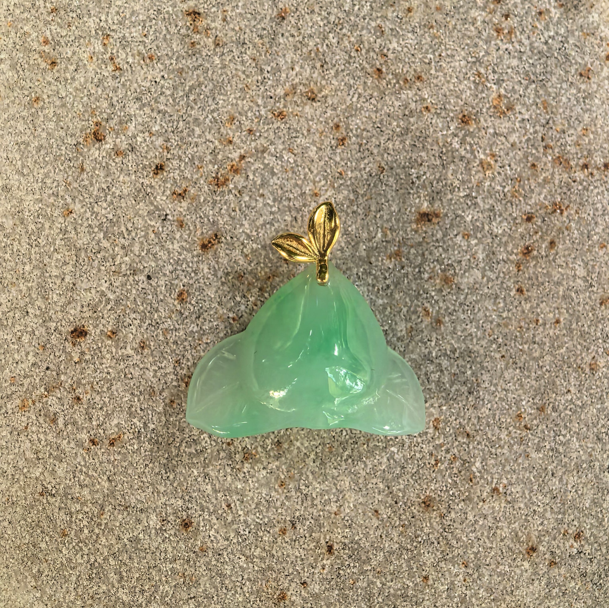 Natural Grade-A green peach jadeite pendant displayed flat with its polished surface and leaf-shaped 18K gold bail.