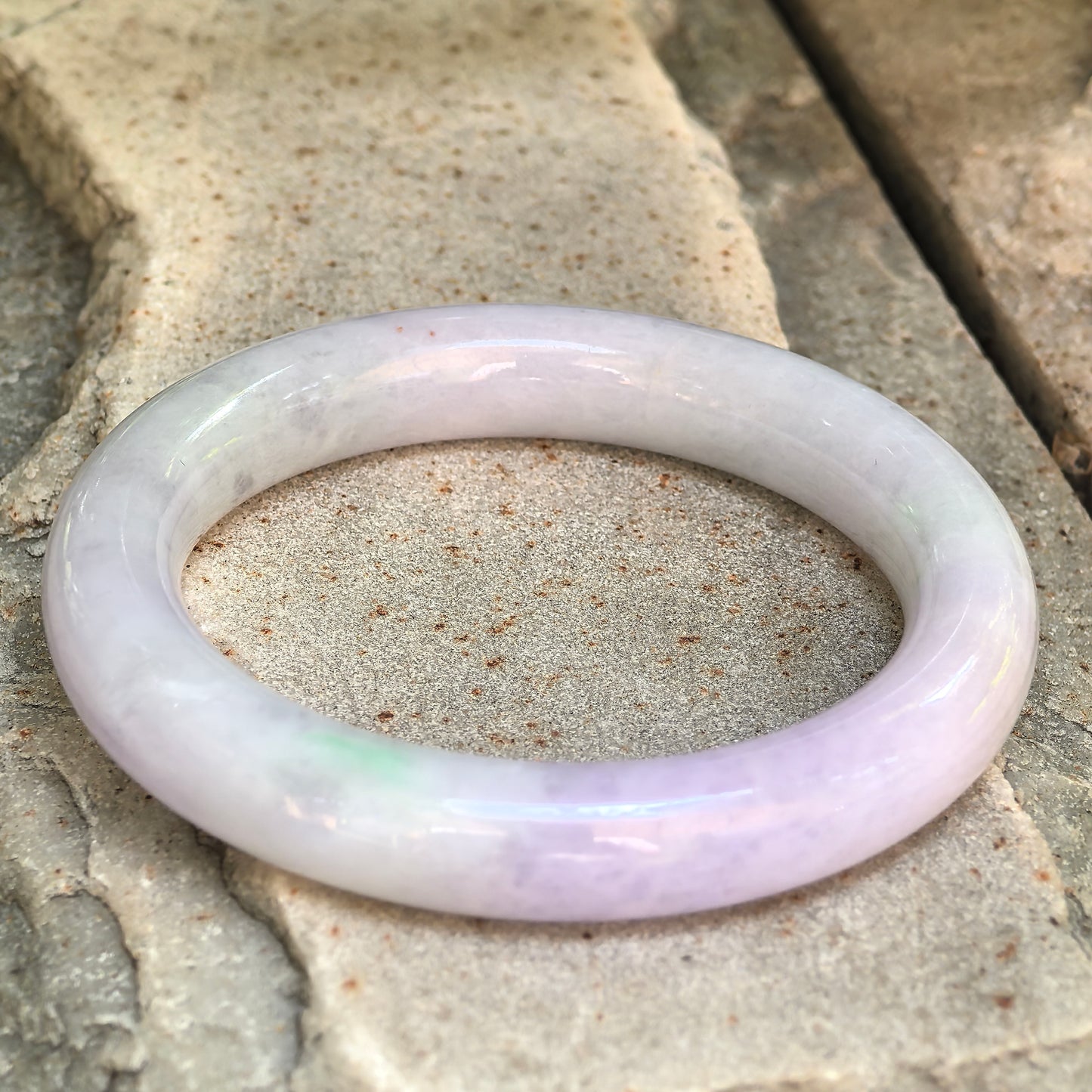 Natural Grade-A light lavender jadeite bangle displayed on a stone surface in natural light.