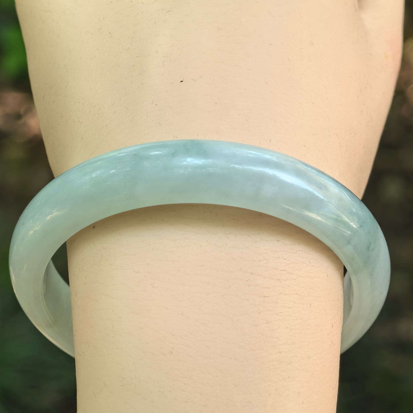 Close-up wrist view of a light green Burmese jadeite bangle showing its smooth glutinous texture.
