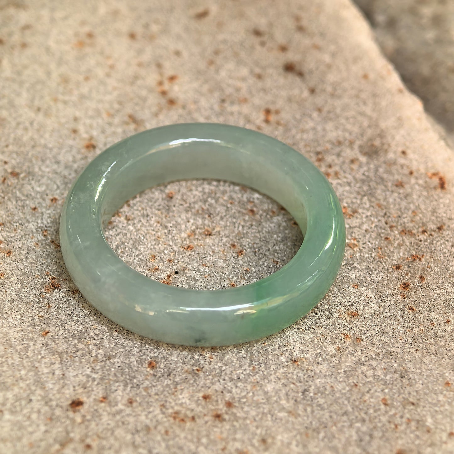 Light green icy glutinous jadeite ring band displayed on stone, showing its polished surface and natural dark inclusion.