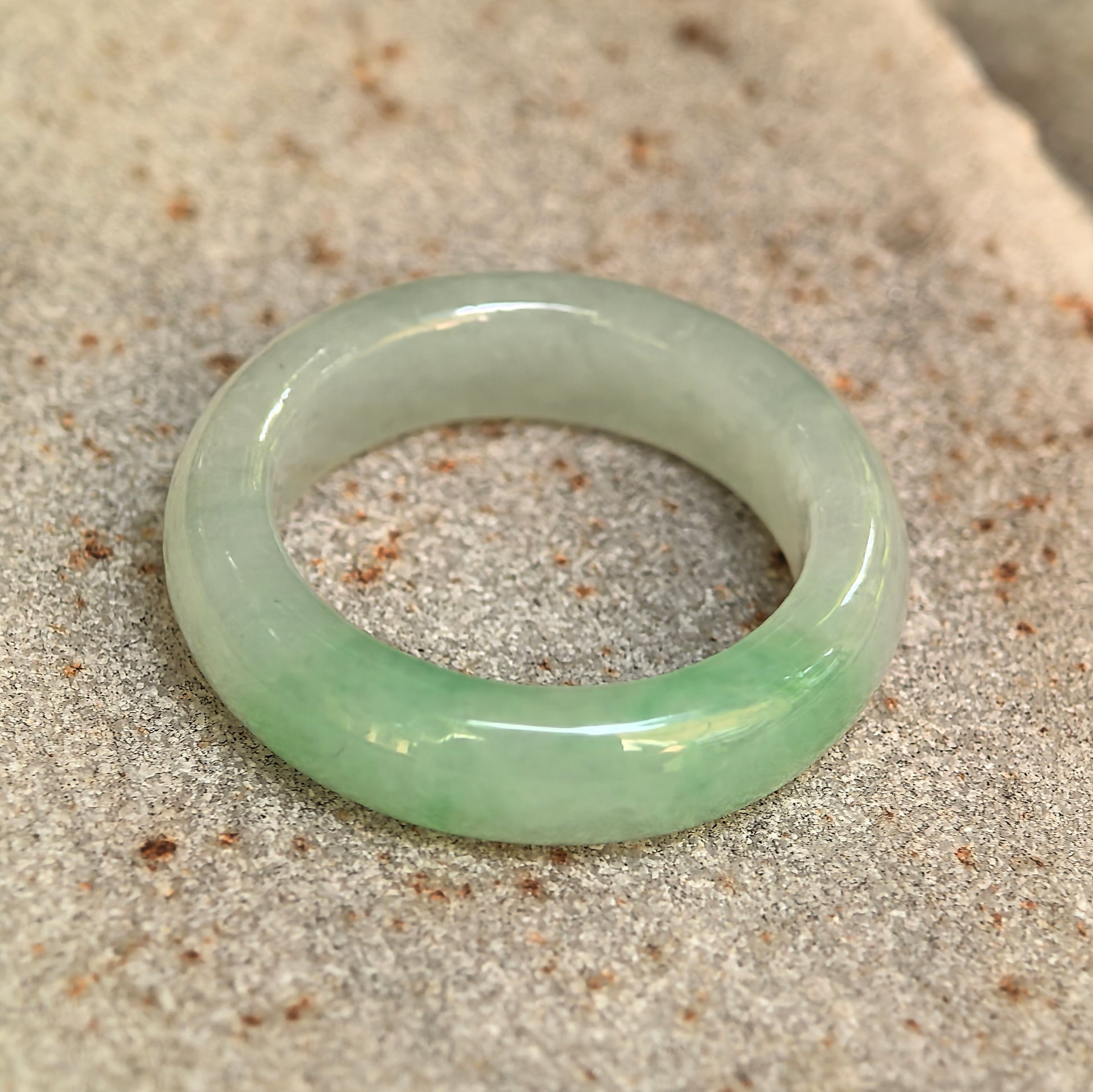 NGTC-certified icy glutinous light green jadeite ring band displayed on stone, showing its smooth polished surface.