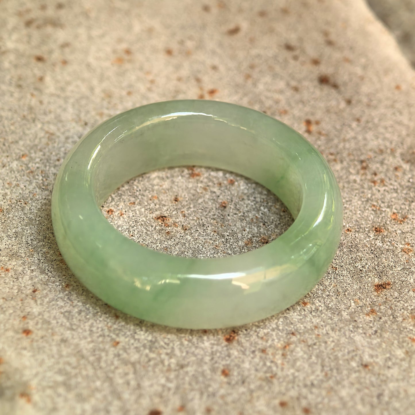 NGTC-certified icy glutinous light green jadeite ring band displayed on stone, showing its substantial thickness and smooth surface.