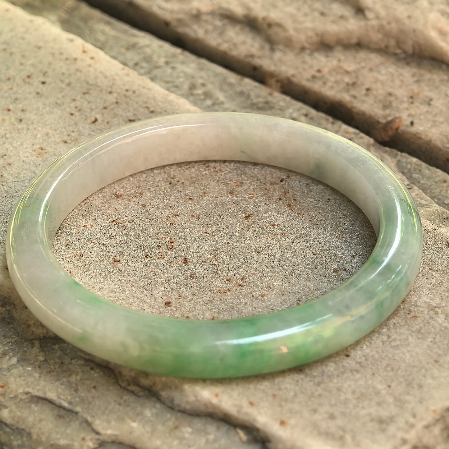Side view showing the slim D-shape profile and polished surface of the jadeite bangle.