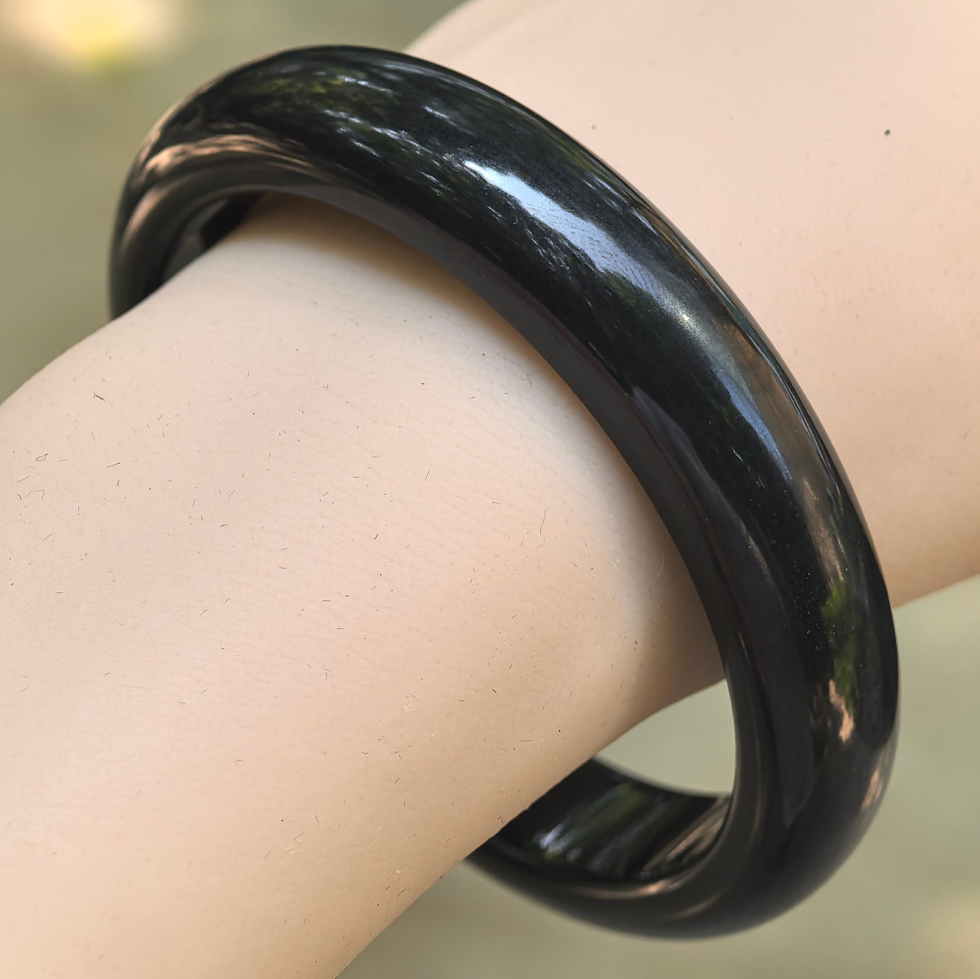 Natural Grade-A glutinous gray-black D-shape jadeite bangle worn on the wrist, showing its smooth polished surface.