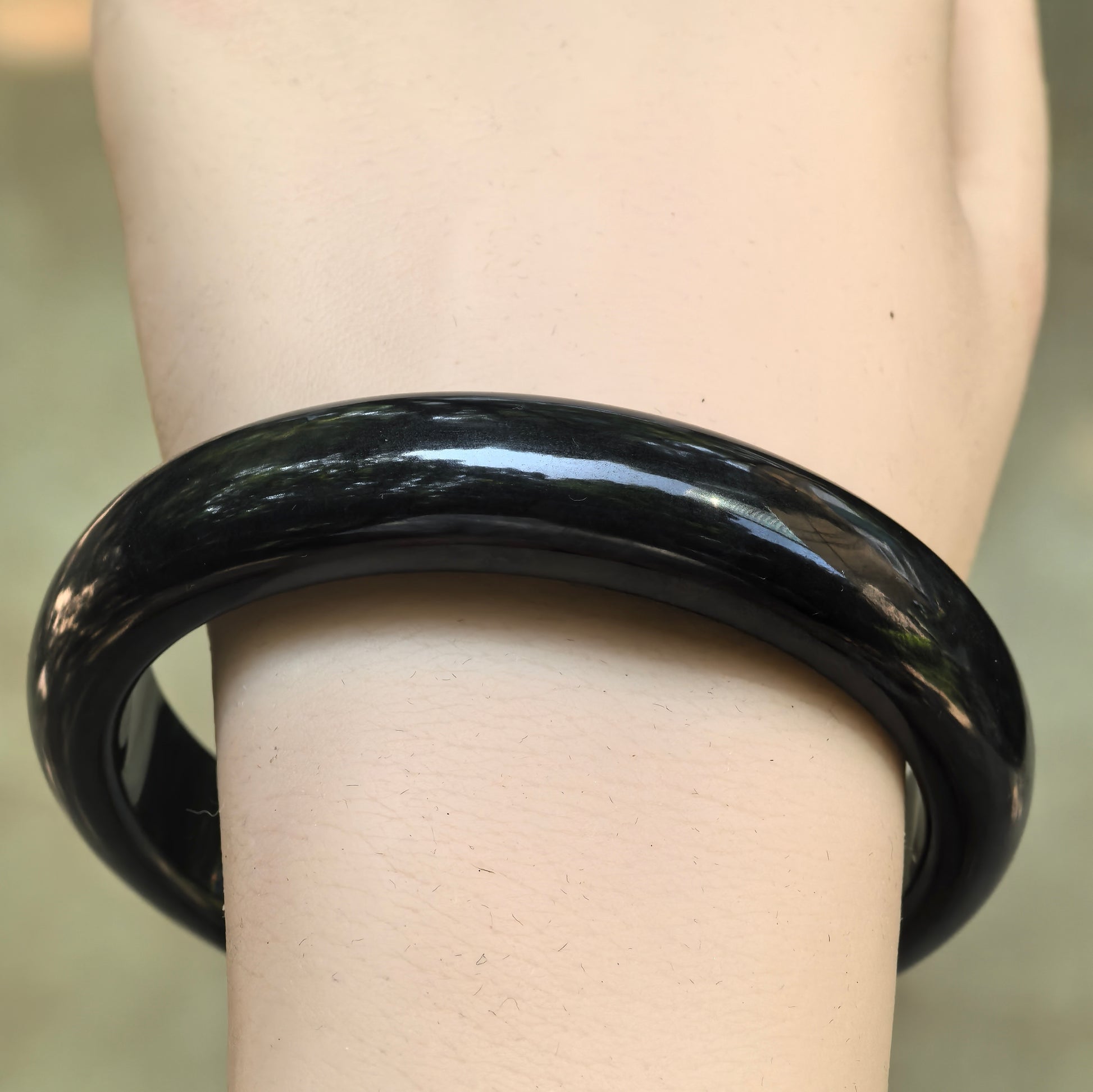 Close-up wrist view of the deep gray-black Burmese jadeite bangle with an even color and glossy luster.