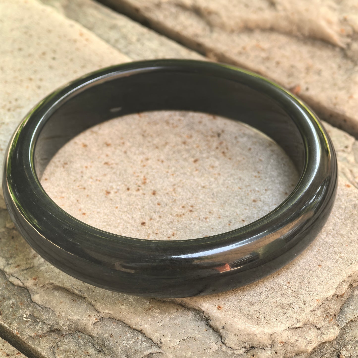 Detailed view of the glutinous gray-black jadeite bangle showing its wide D-shape profile and natural texture.