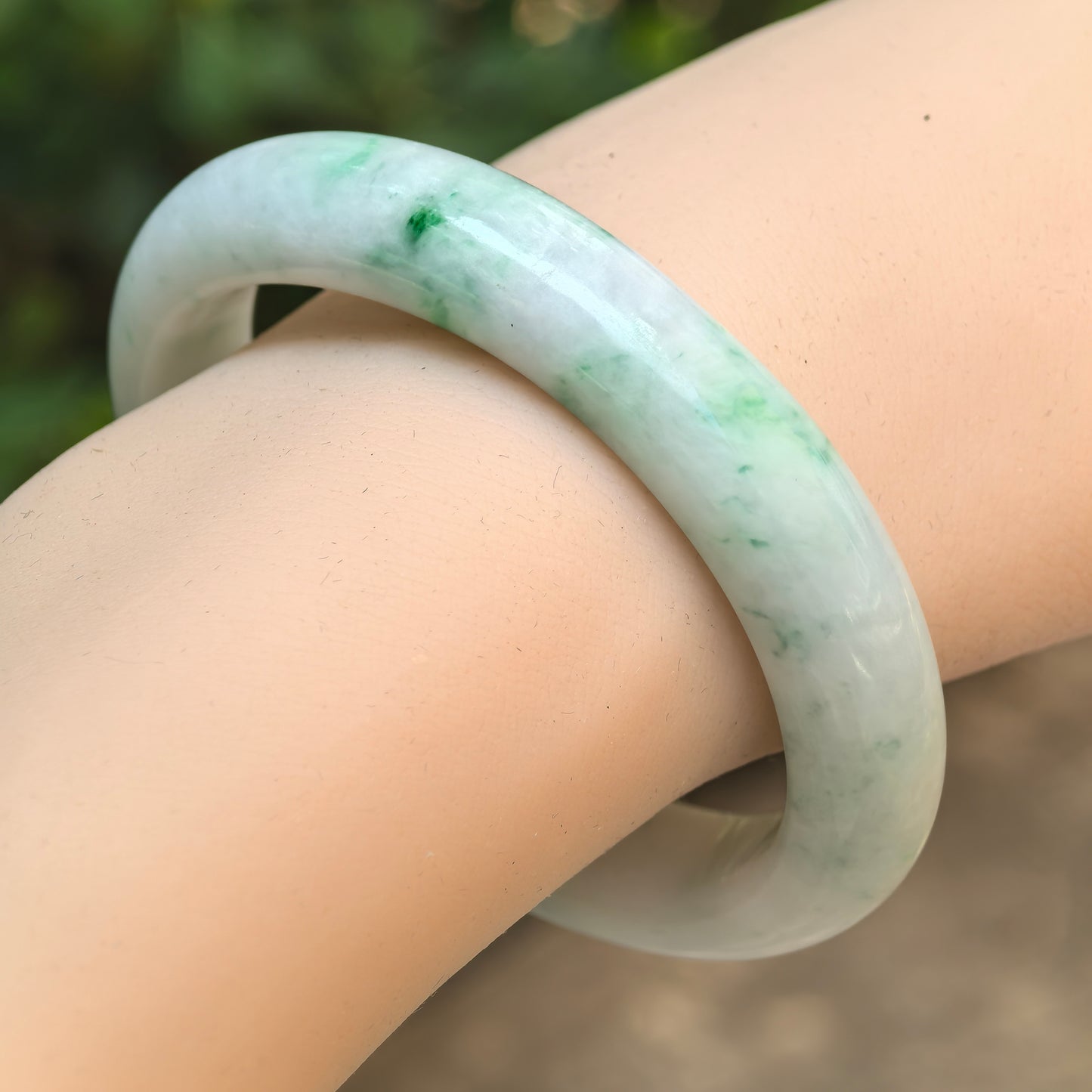 Natural Grade-A glutinous white-base green oval jadeite bangle worn on the wrist, showing vivid green accents.