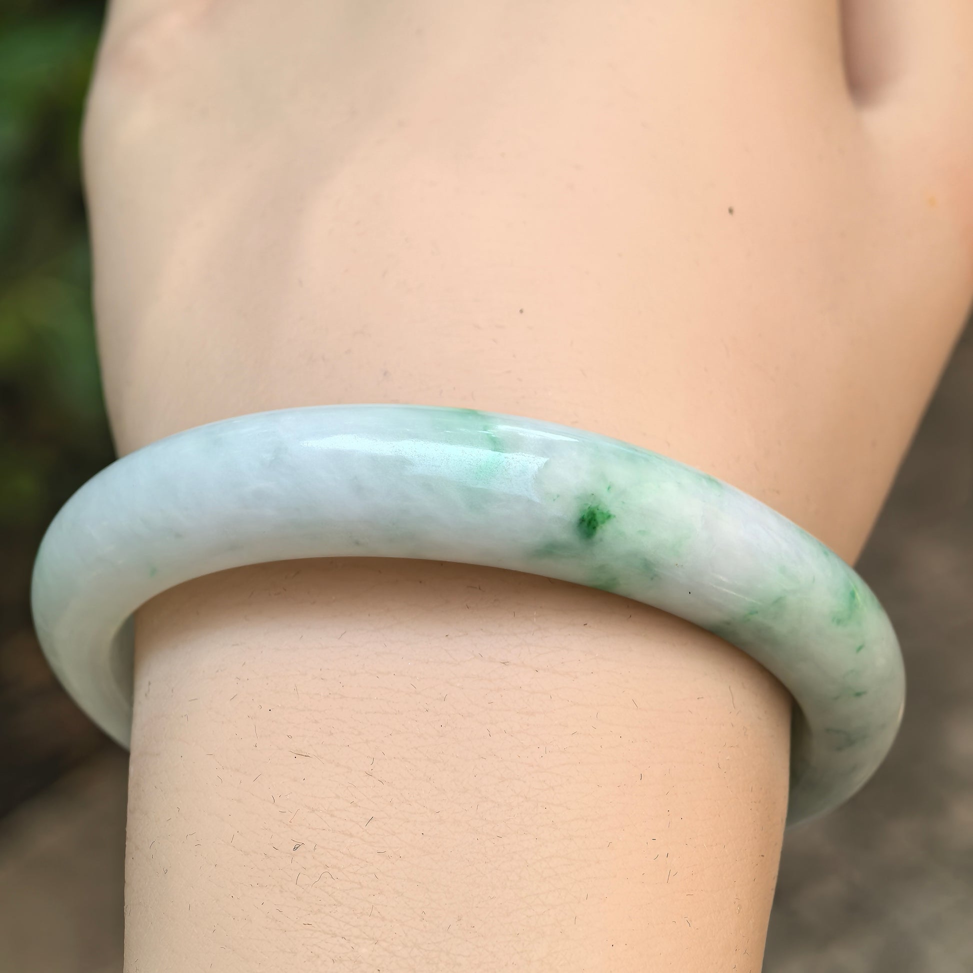 Wrist view of the white-base green Burmese jadeite bangle with a smooth polished surface and glutinous texture.