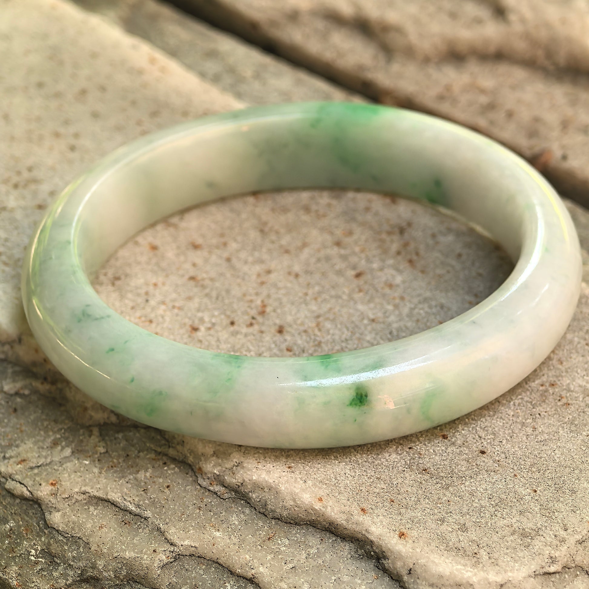 Detailed angled view of the oval jadeite bangle showing its bright green patches and soft white base.