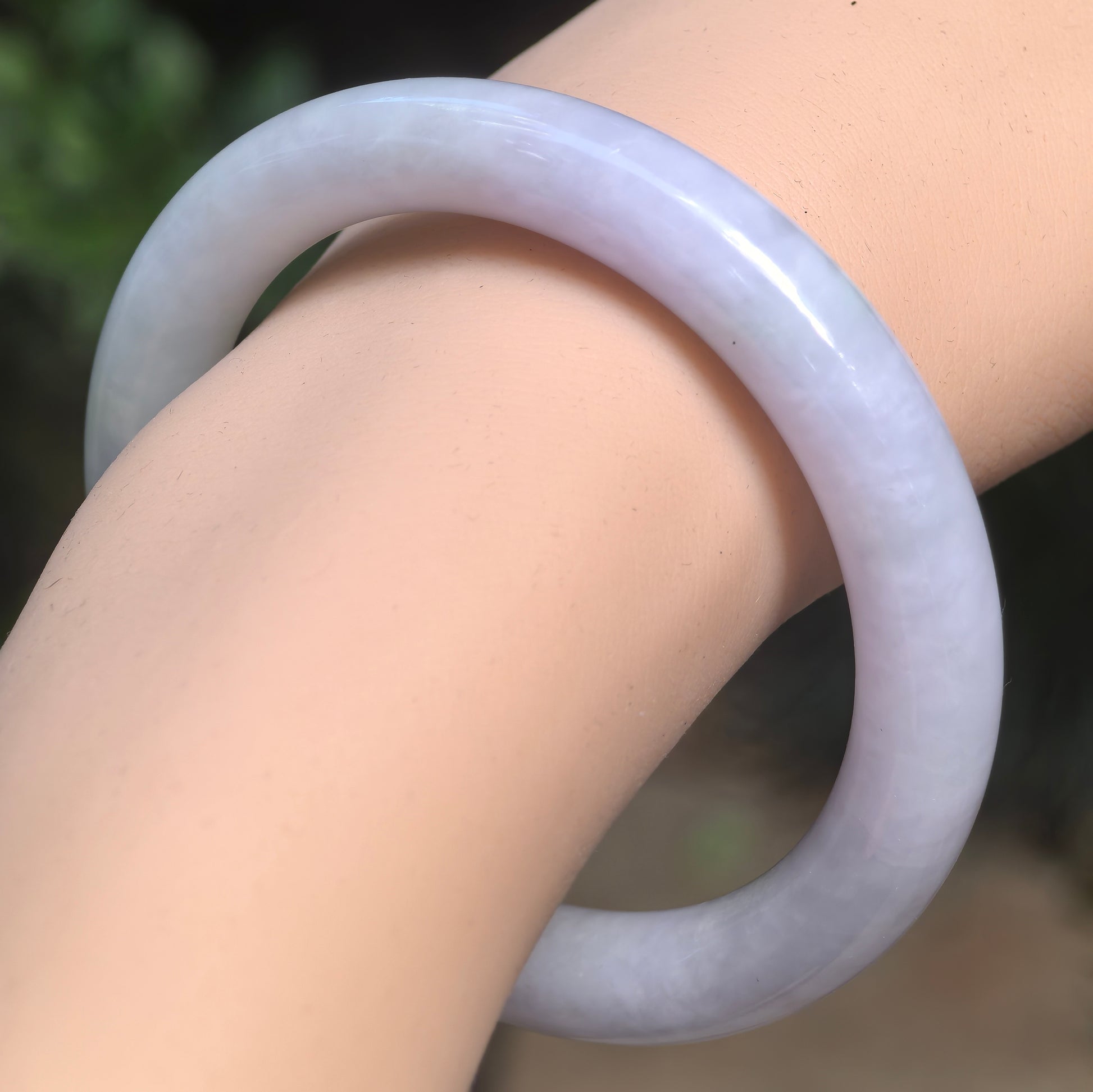 Natural Grade-A glutinous pale lavender-green round-bar jadeite bangle worn on the wrist in soft indoor light.