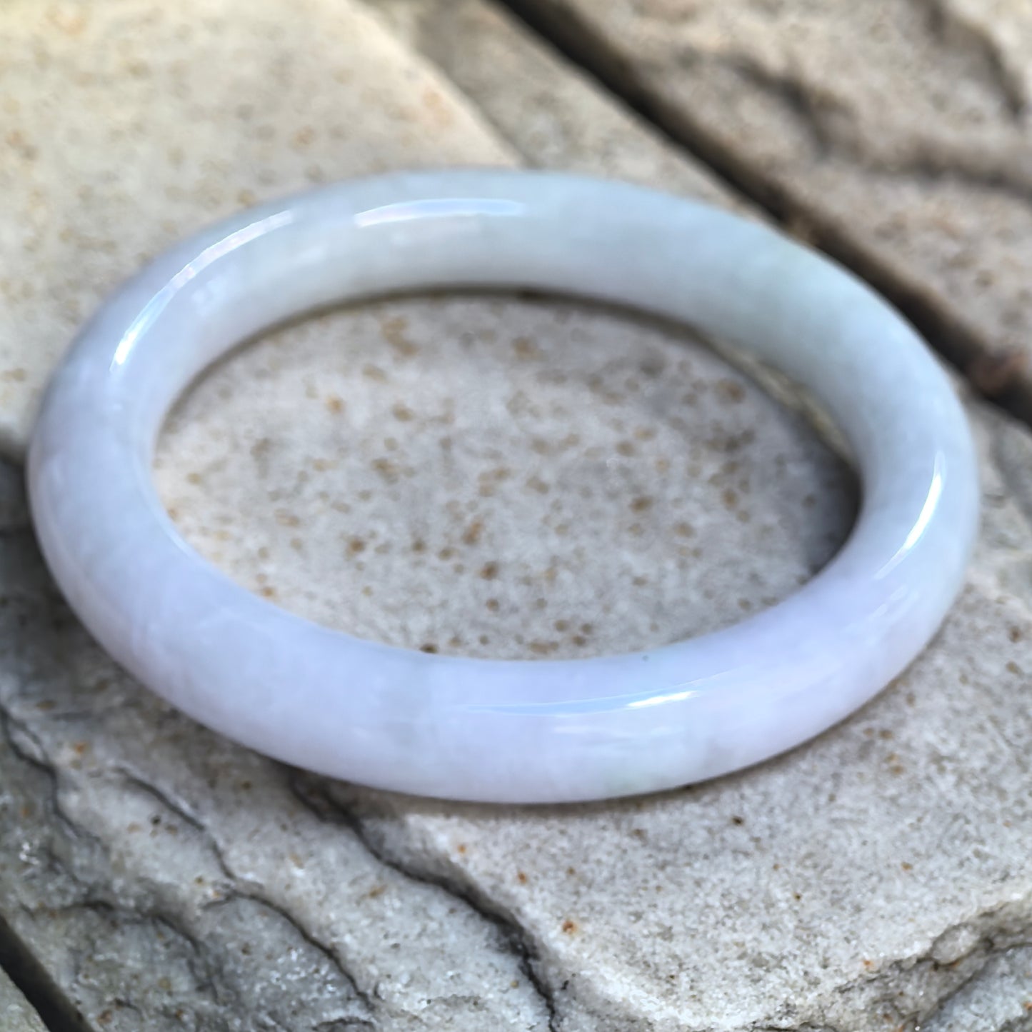 Angled detail view of the glutinous pale lavender and light green jadeite bangle on a natural stone surface.
