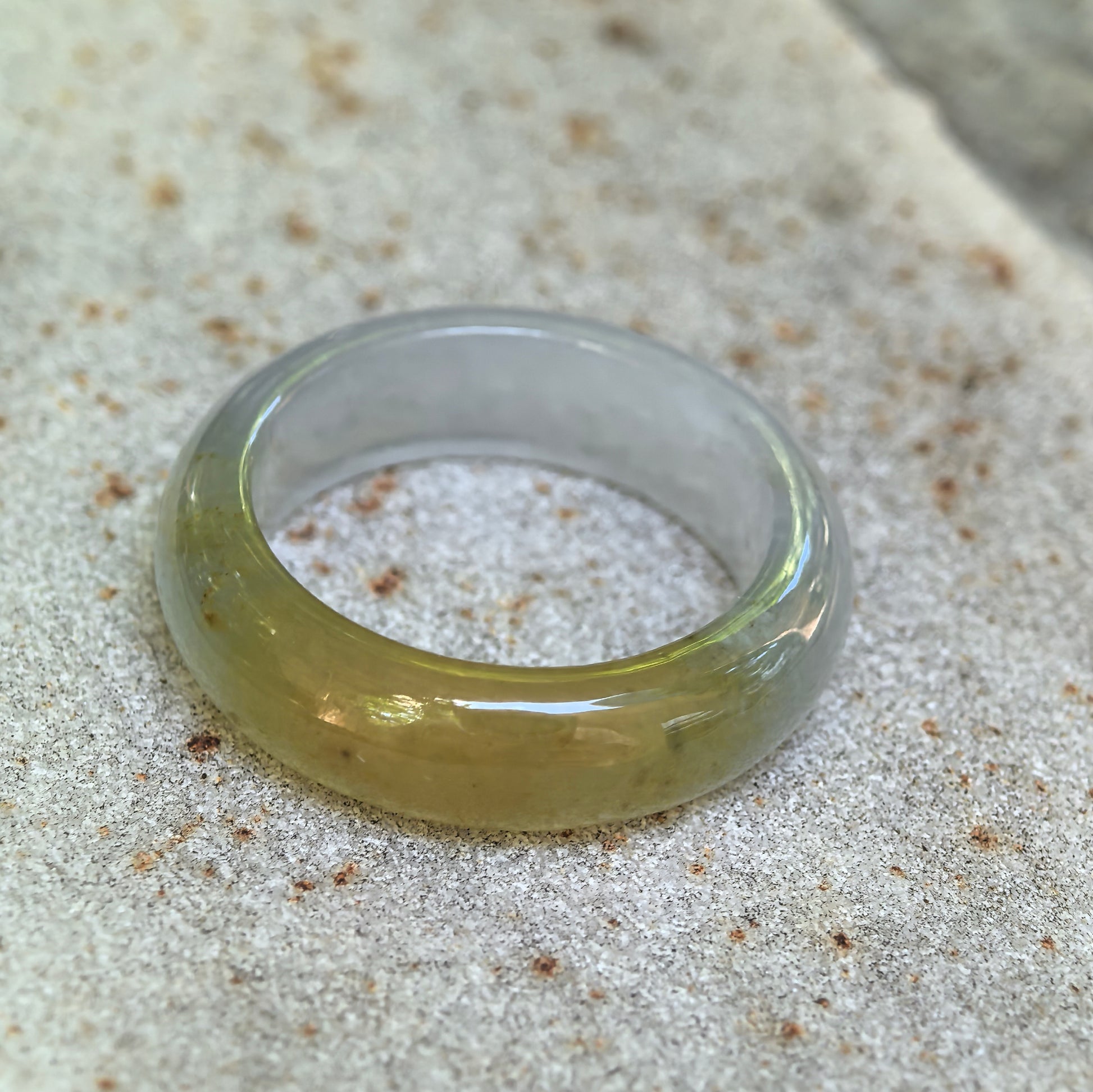 Angled detail view of the natural Grade-A jadeite ring band resting on a stone surface with a polished domed exterior.