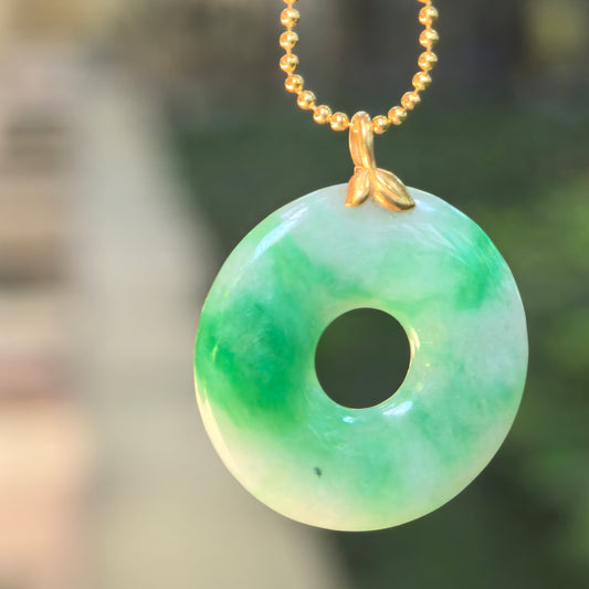 Natural Grade-A glutinous white-base green donut jadeite pendant hanging from a chain with an 18K gold leaf-shaped bail.