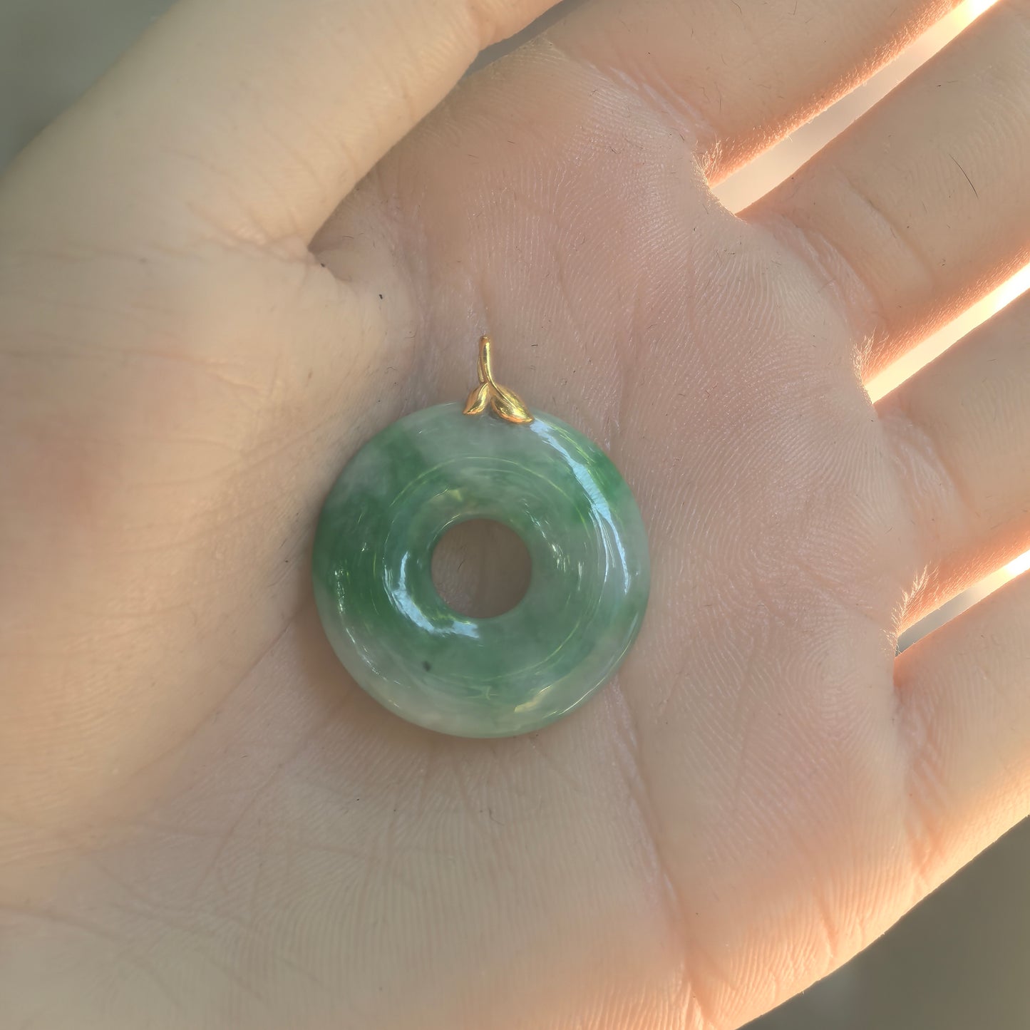 Hand-held view of the white-base green jadeite donut pendant showing its rounded profile and natural black spot.