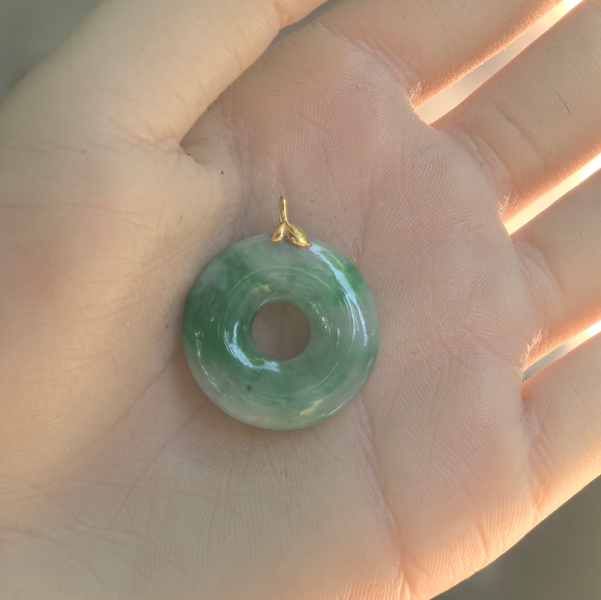 Hand-held view of the white-base green jadeite donut pendant showing its rounded profile and natural black spot.