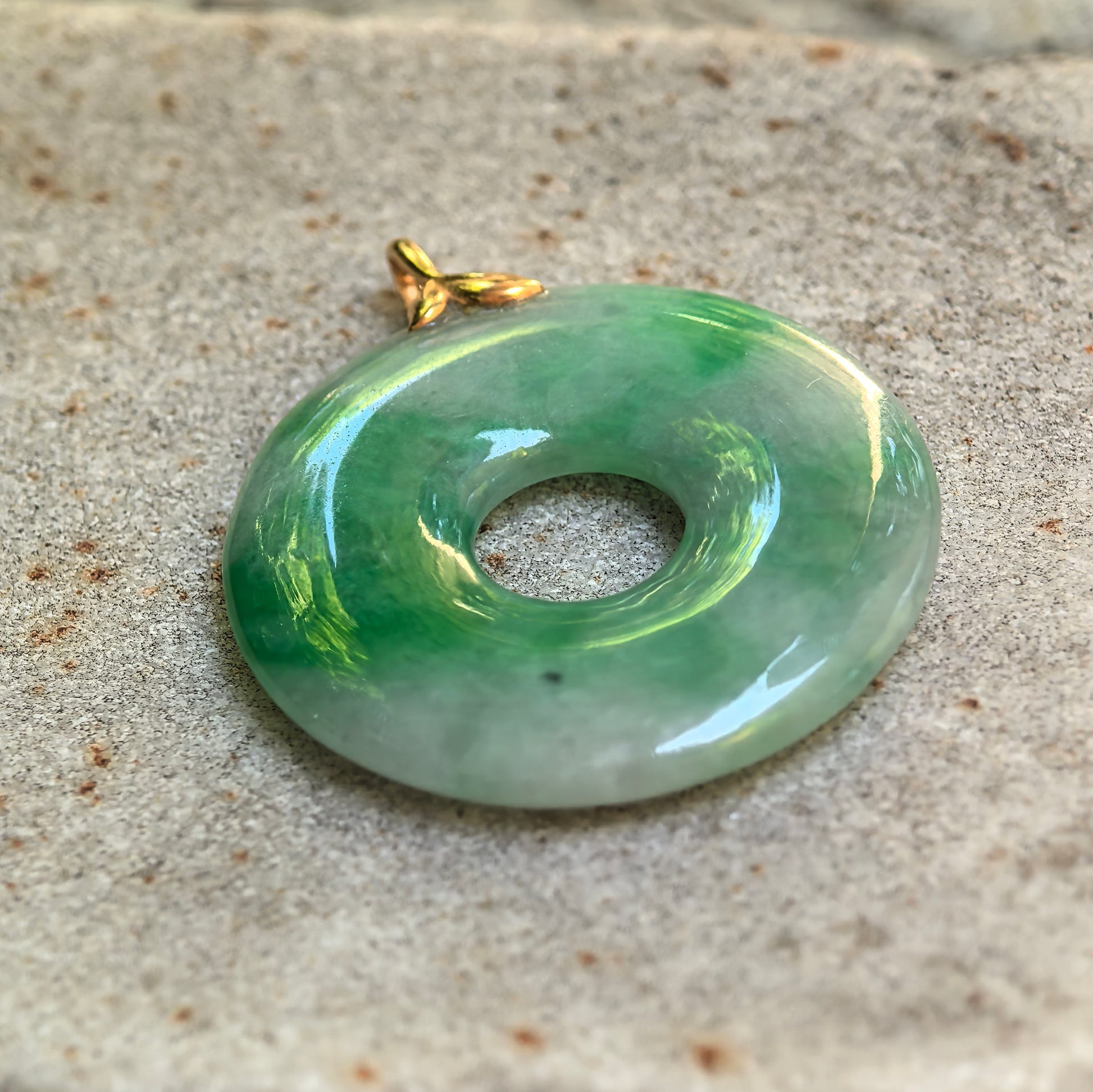 Close-up of the glutinous green jadeite donut pendant showing concentrated green color, smooth polish and central opening.