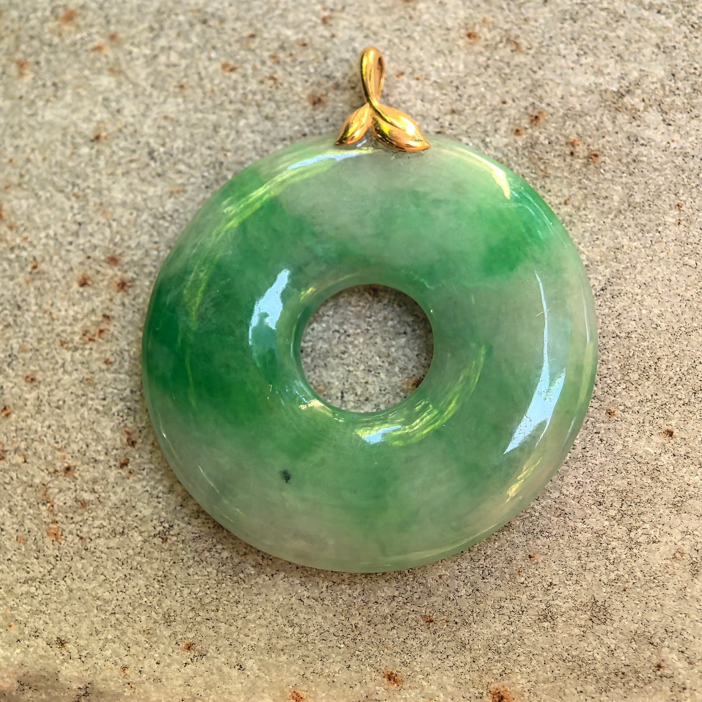 Front view of the natural jadeite donut pendant showing its white-and-green color distribution and 18K gold bail.