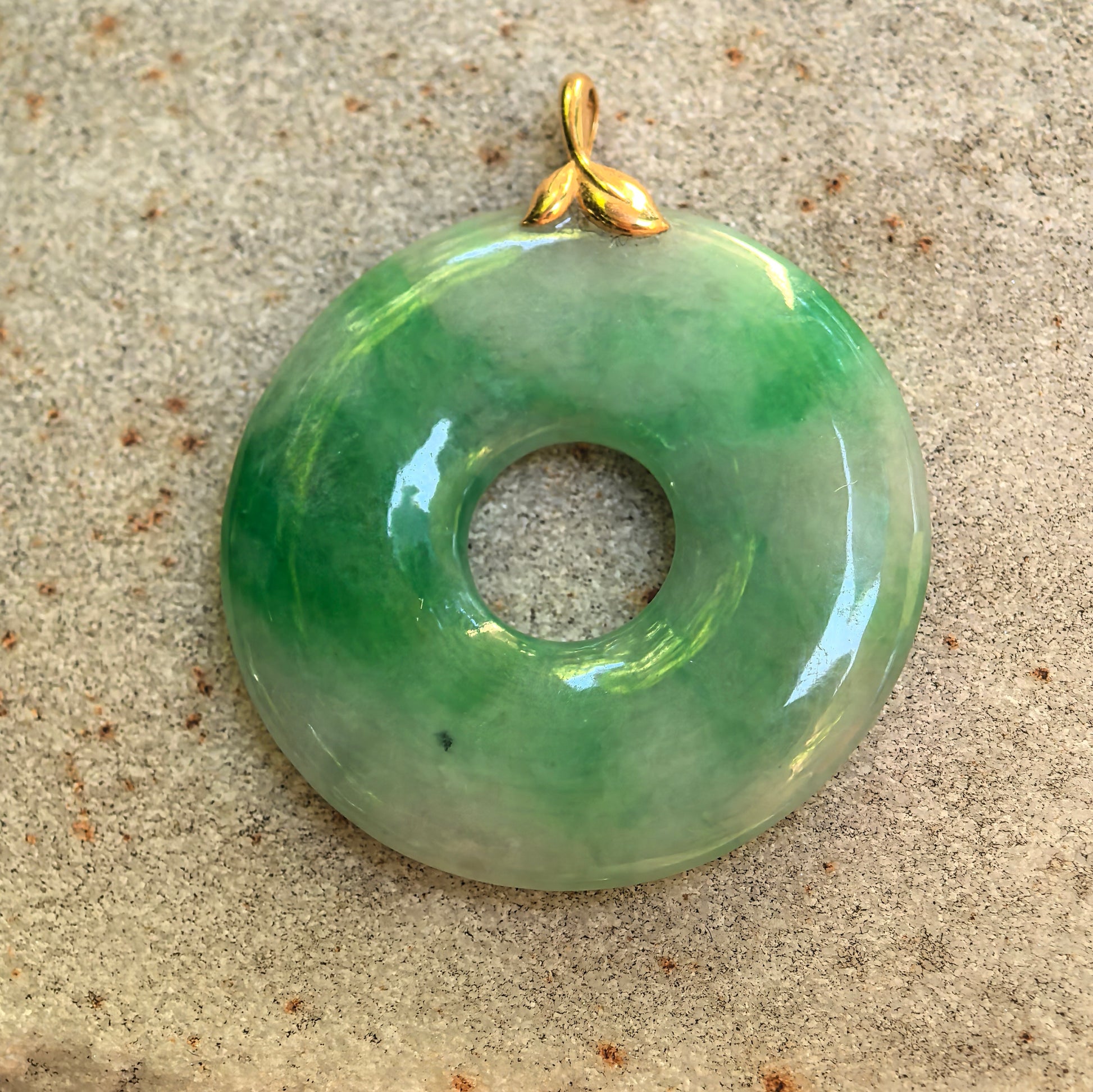 Front view of the natural jadeite donut pendant showing its white-and-green color distribution and 18K gold bail.