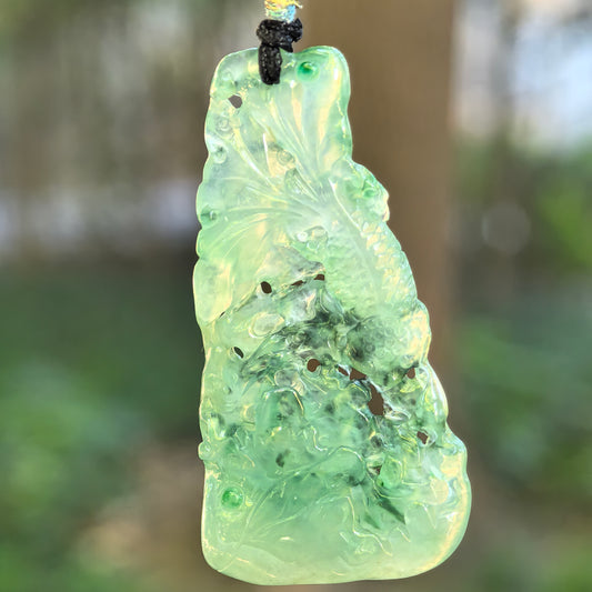 Natural Grade-A icy green lotus and fish jadeite pendant hanging from a black cord in natural light.
