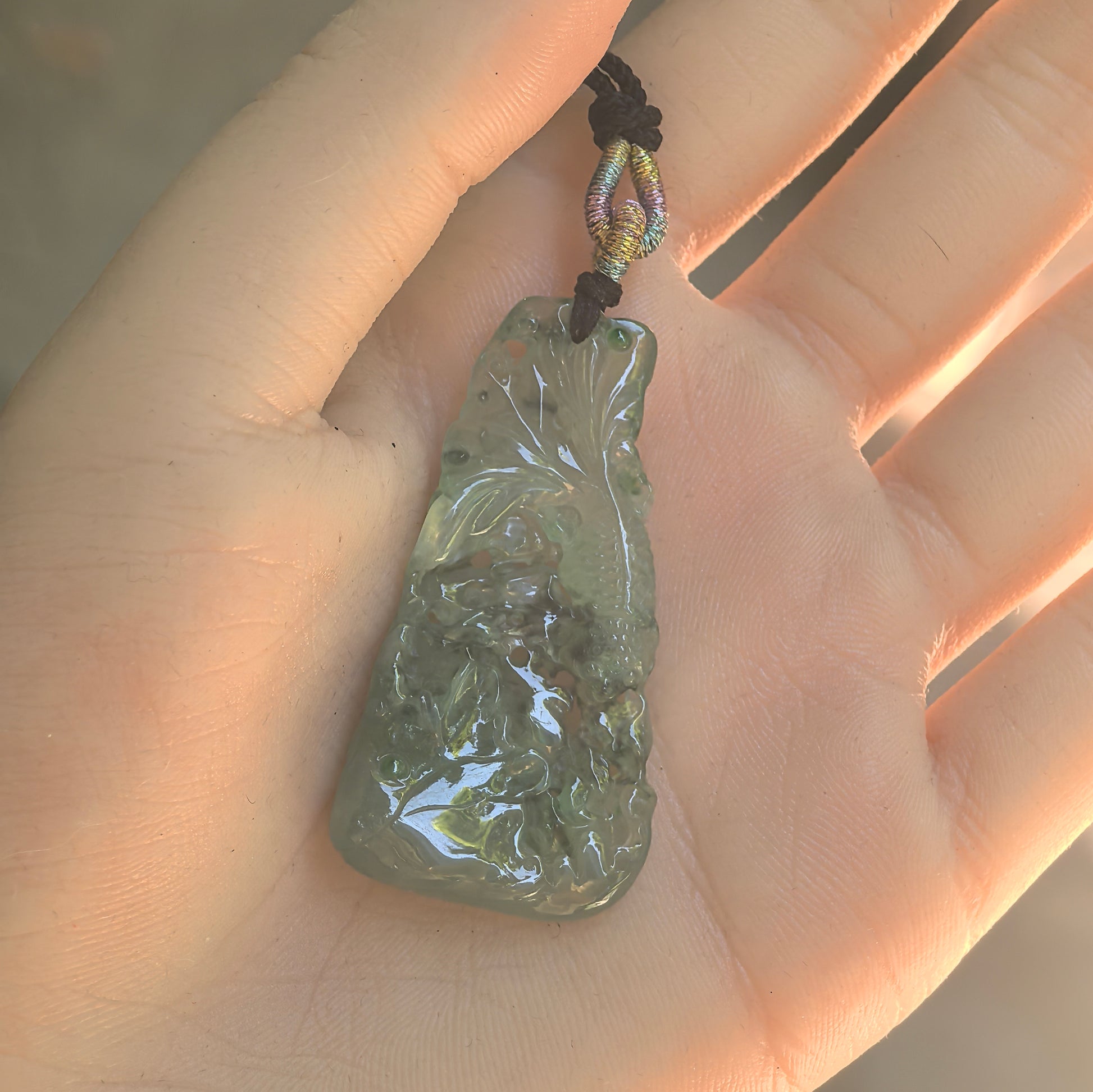 Backlit view of the light green Burmese jadeite pendant showing its translucency and detailed openwork carving.