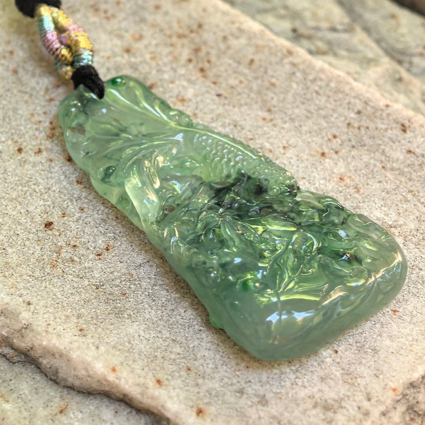 Close-up side view of the green lotus and fish jadeite pendant showing its substantial thickness and layered craftsmanship.