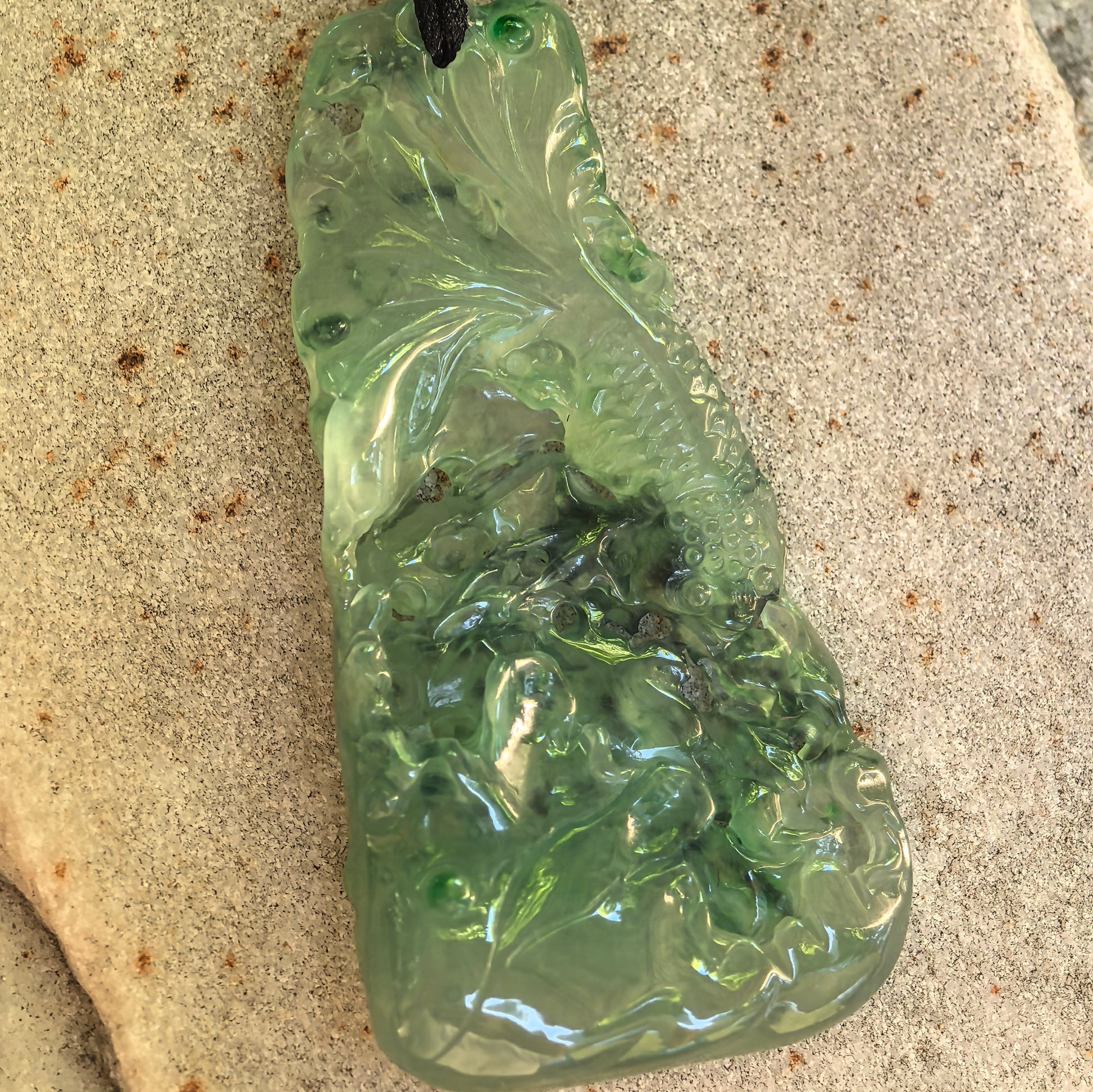 Front detail of the icy green jadeite pendant showing the carved fish, lotus leaves, flowers, and openwork sections.