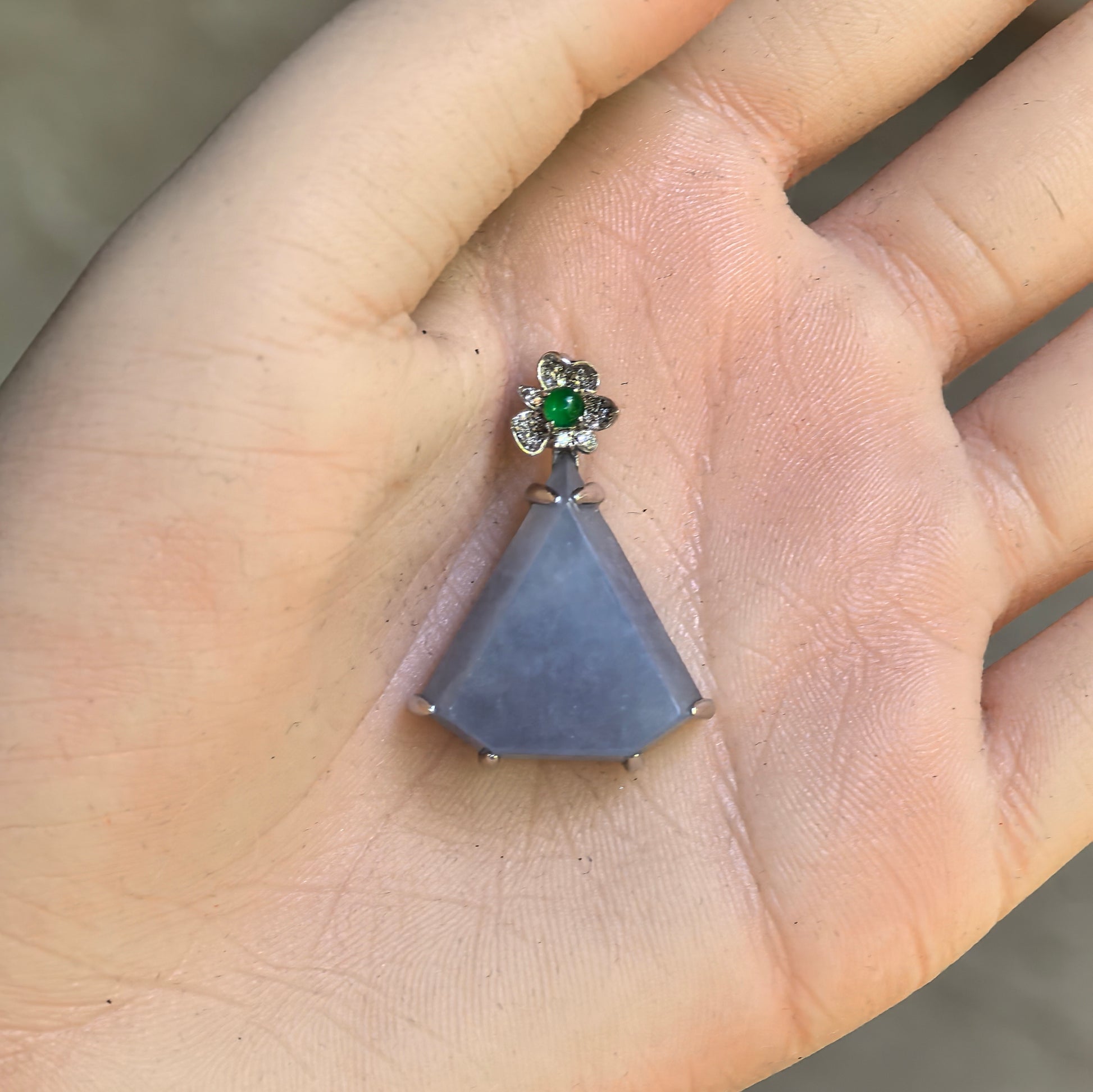 Hand-held view of the rich lavender jadeite triangle pendant showing its substantial size, thick profile, and floral 18K gold setting.
