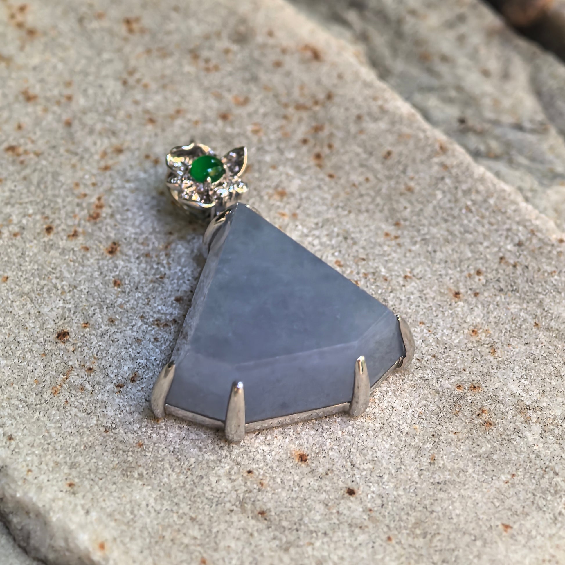 Angled detail view of the faceted lavender jadeite pendant showing its polished surface, triangular shape, and secure metal prongs.