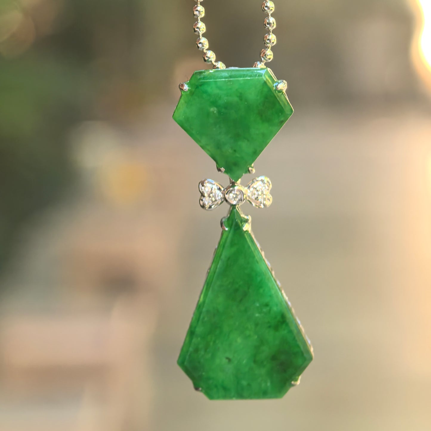 Natural Grade-A icy glutinous rich green bow-tie jadeite pendant hanging from a chain with an articulated geometric design.
