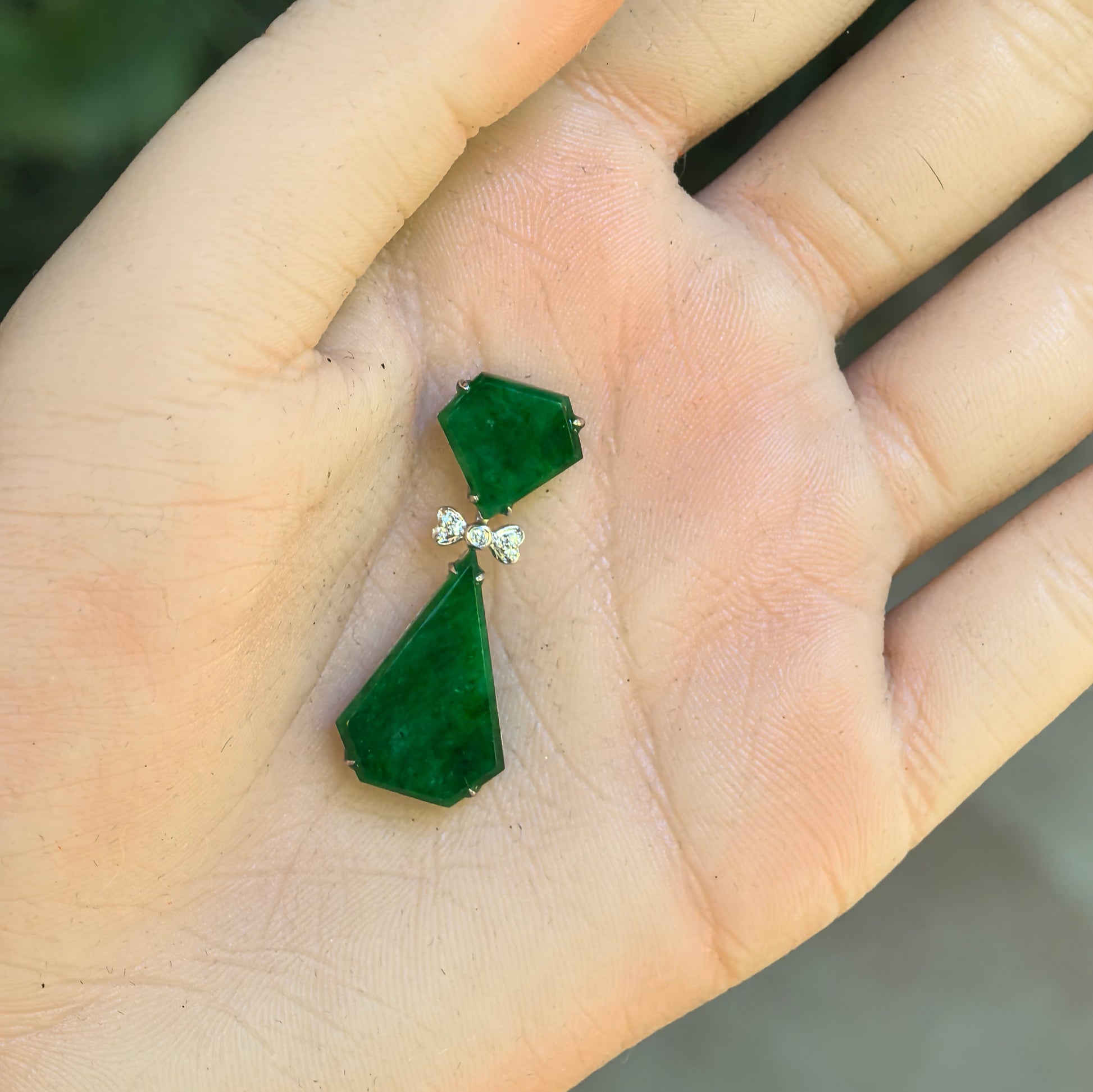 Hand-held view of the rich green jadeite pendant showing two geometric sections connected by a diamond bow.