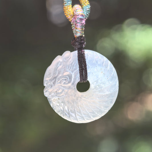 Natural Grade-A icy white dragon round jadeite pendant hanging from its woven cord in natural backlight.