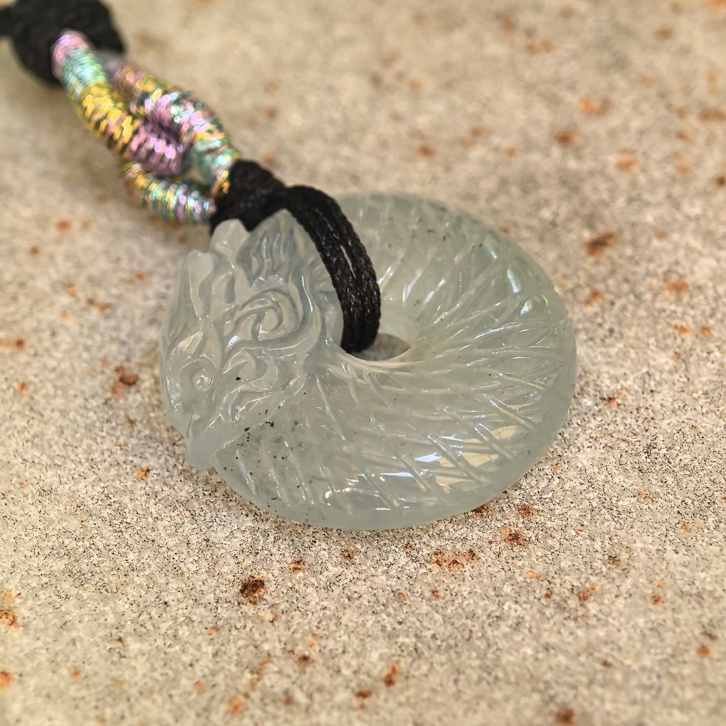 Angled view of the icy white Burmese jadeite pendant showing the open center, dragon carving, and gel-like translucency.