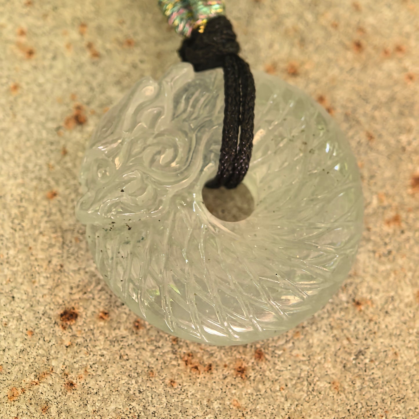 Close-up of the white jadeite dragon pendant showing detailed scales, flowing carving, and small natural mineral inclusions.