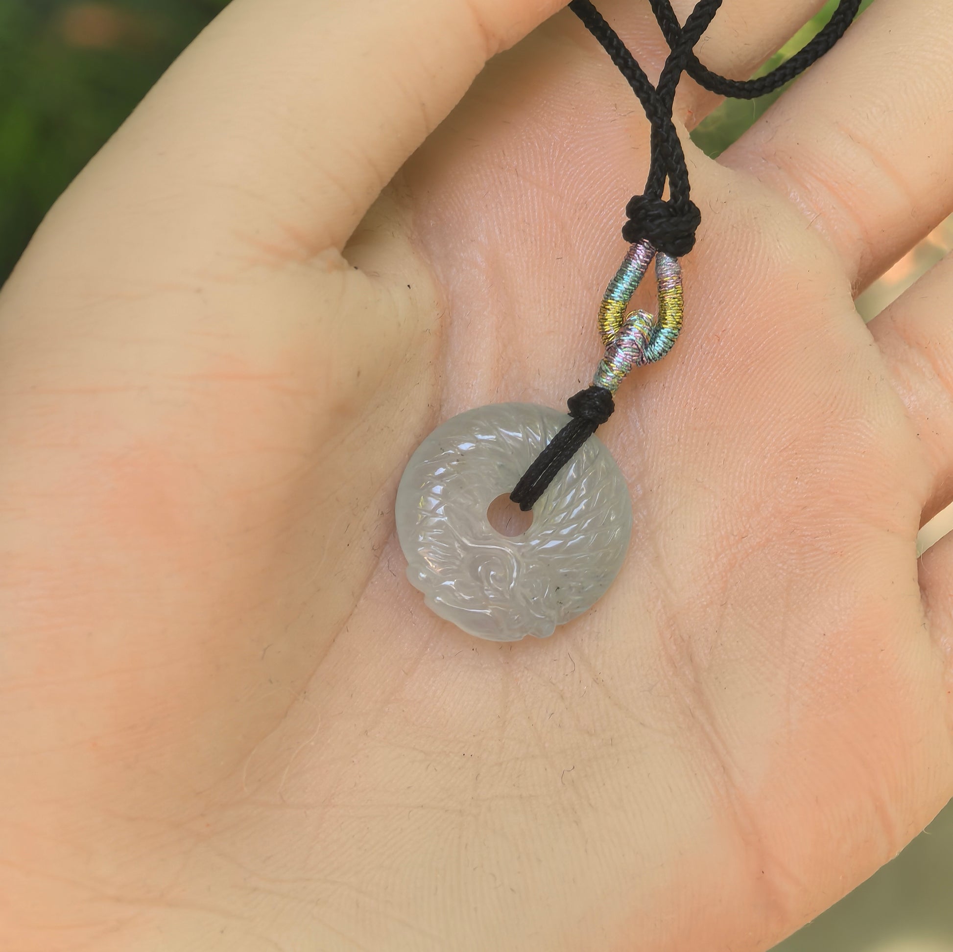 Natural Grade-A icy white dragon round jadeite pendant displayed in the hand to show its compact size and carved design.