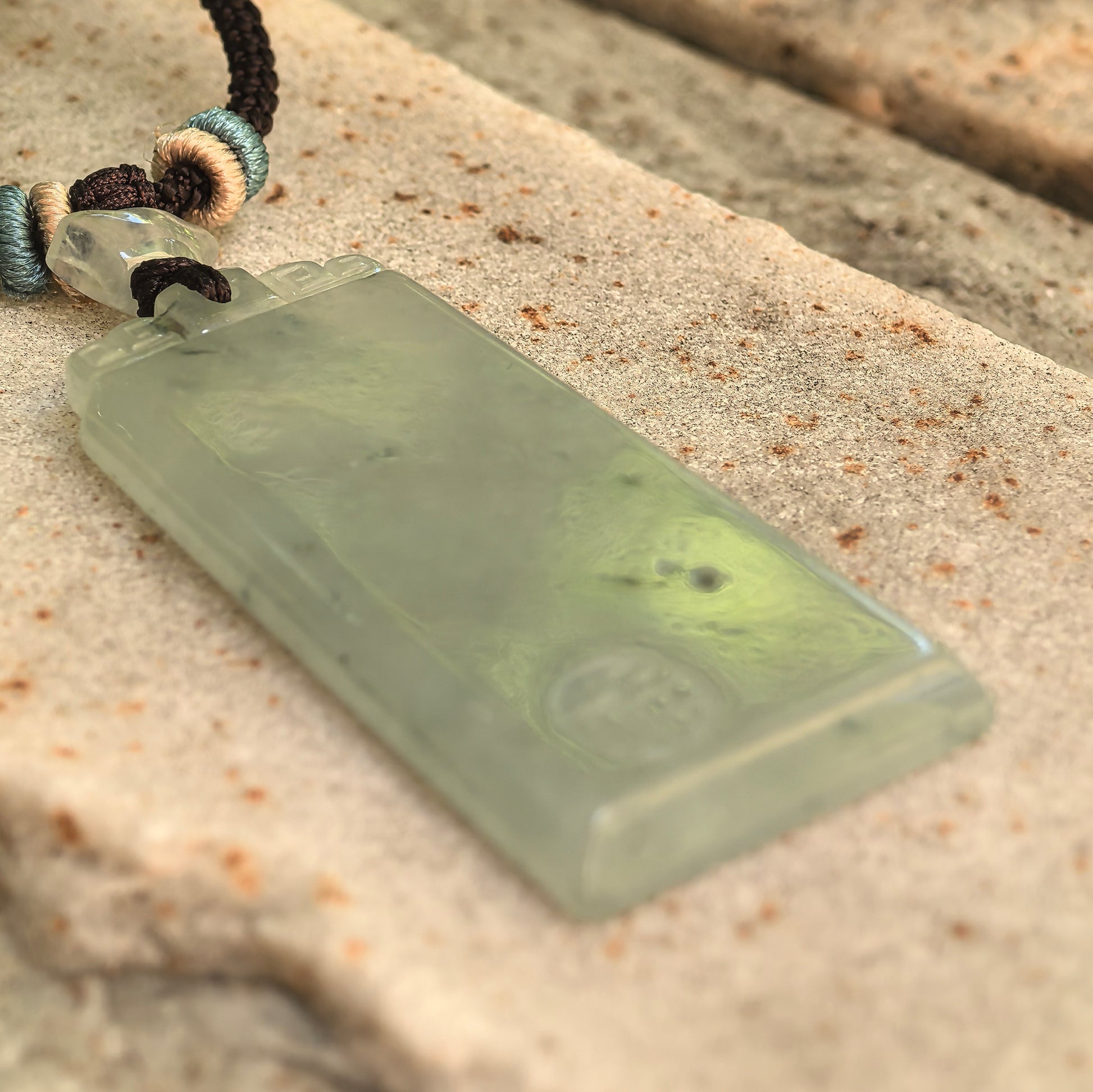 Side view of the light green Burmese jadeite plain plaque pendant showing its polished border, thickness, and deep green floating patterns.