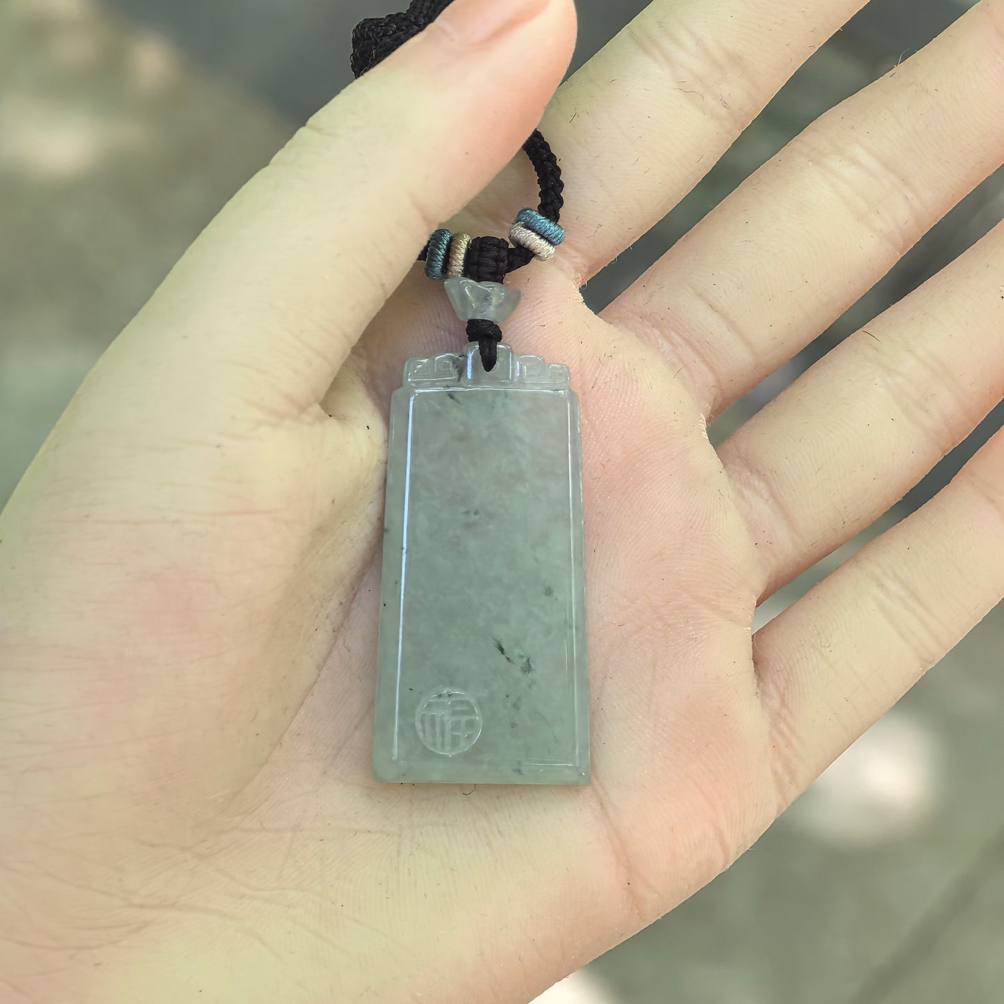 Natural Grade-A light green jadeite plain plaque pendant displayed in the hand to show its size and elongated shape.