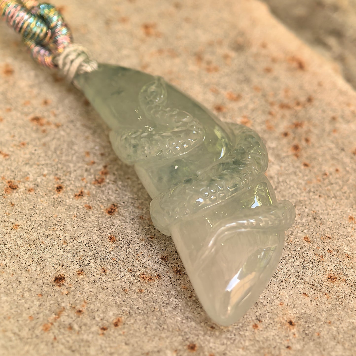 Angled view of the light green Burmese jadeite snake pendant showing its curved three-dimensional structure and good translucency.