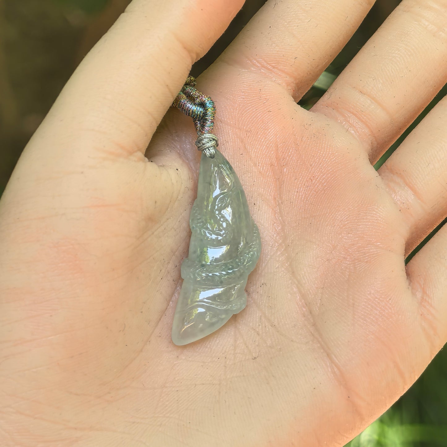 Natural Grade-A light green snake jadeite pendant displayed in the hand to show its elongated size and detailed carving.