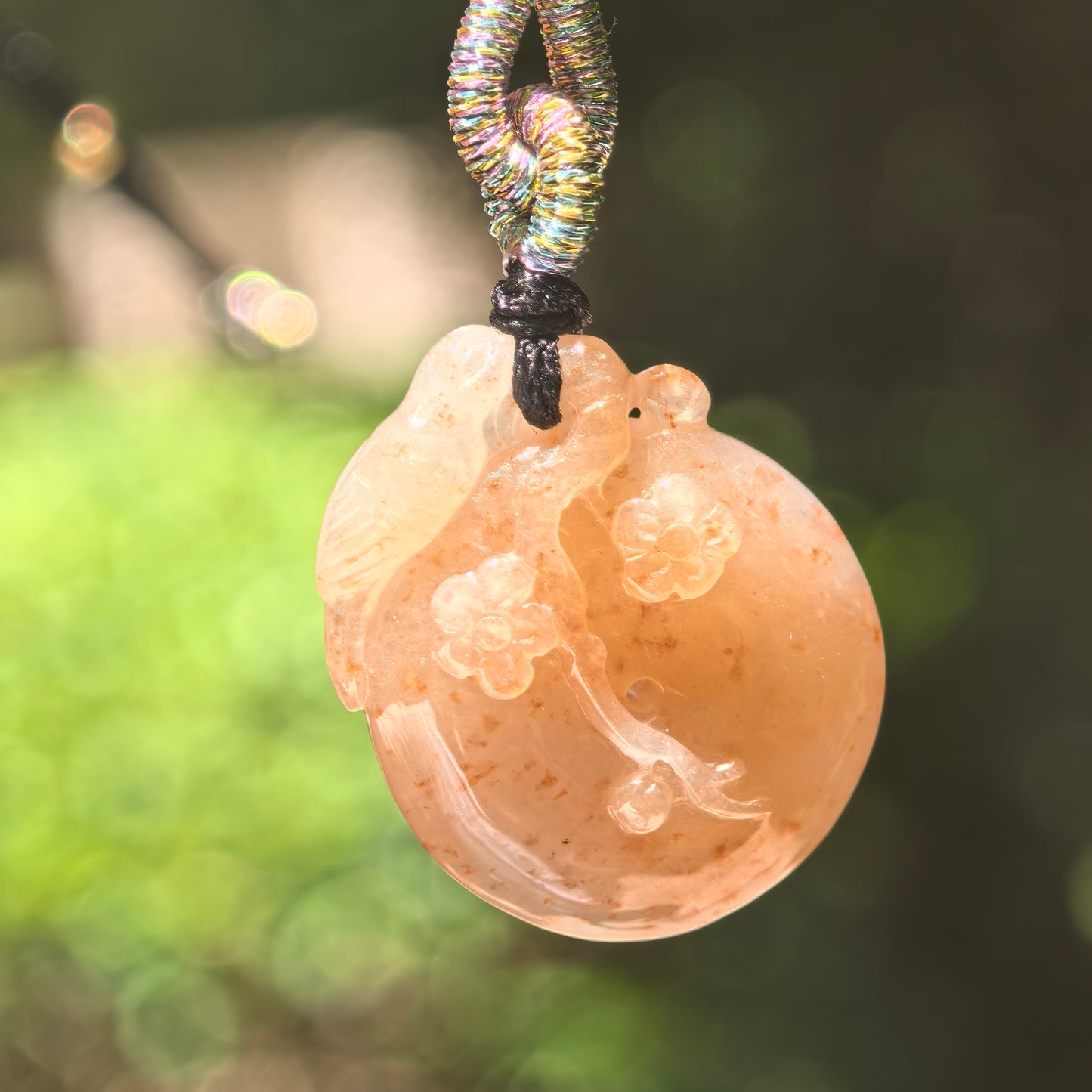 Natural Grade-A glutinous warm yellow plum blossom jadeite pendant hanging from its woven cord in natural light.