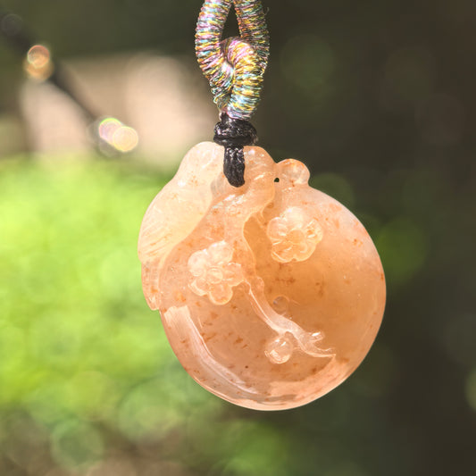 Natural Grade-A glutinous warm yellow plum blossom jadeite pendant hanging from its woven cord in natural light.