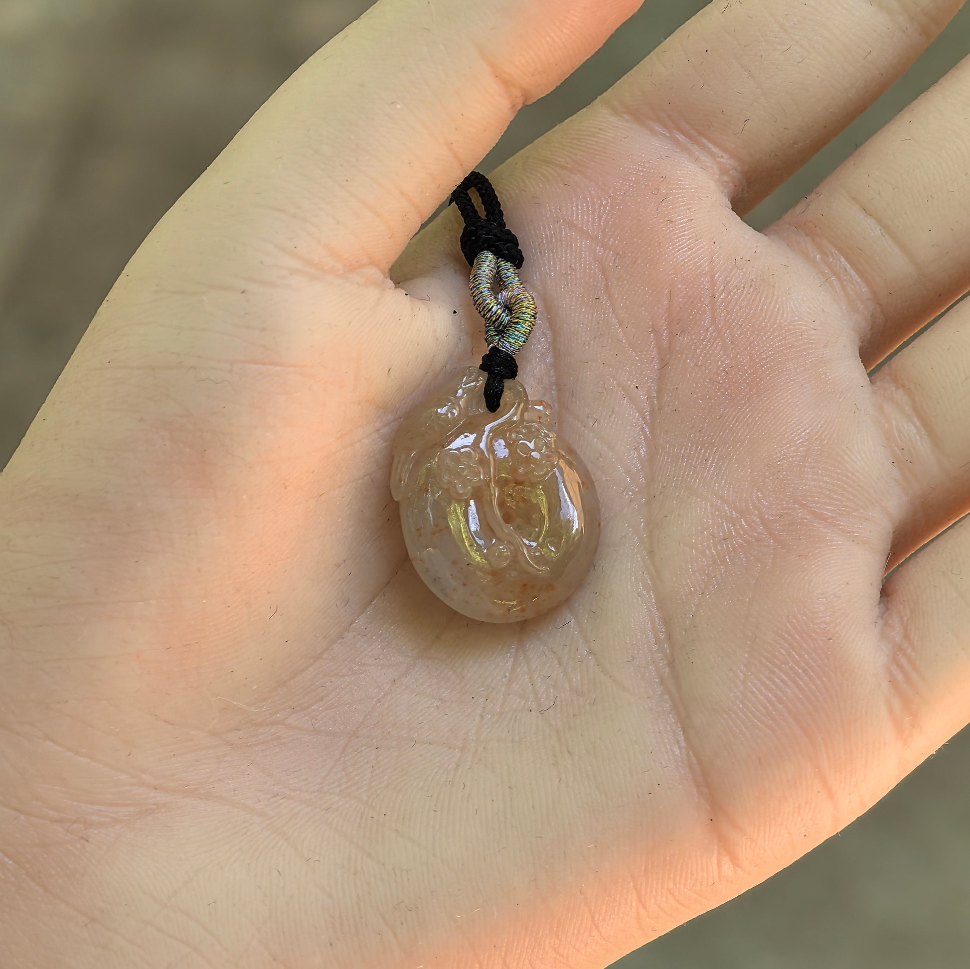 Natural Grade-A yellow plum blossom jadeite pendant displayed in the hand to show its compact rounded size and carved design.
